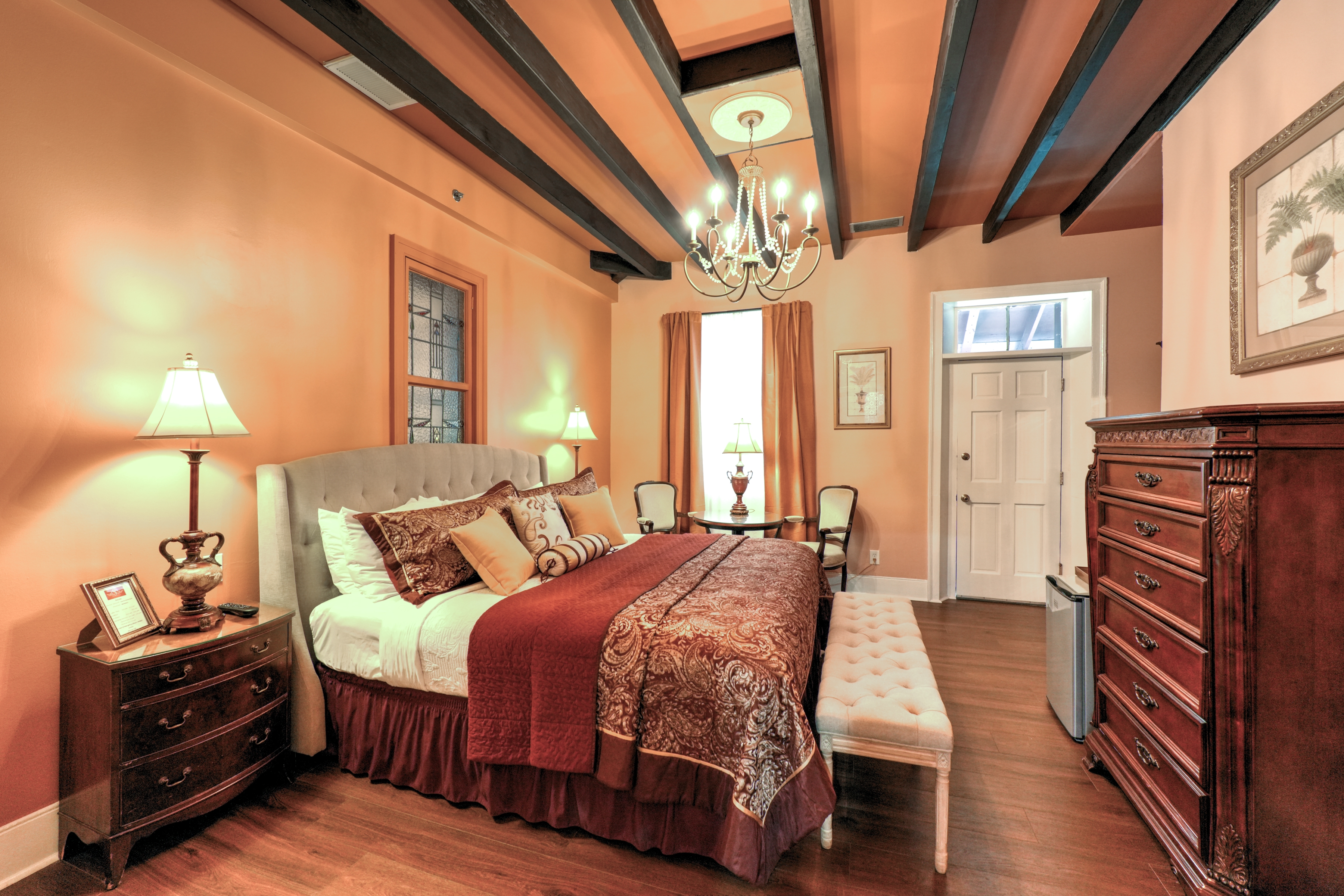 Warm and inviting bedroom with beam ceiling and richly decorated with a king bed, antique furniture and lovely artwork