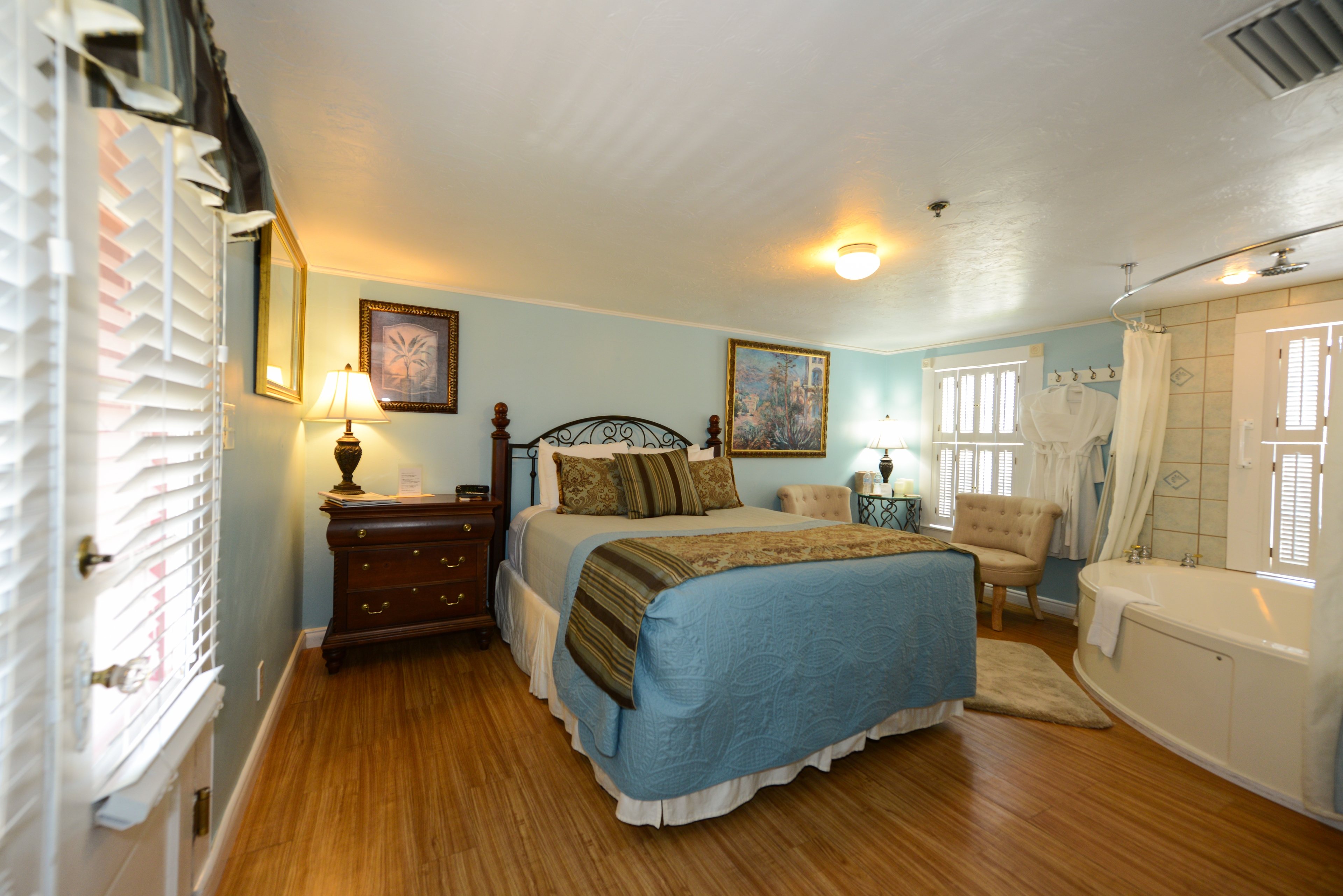 Romantic corner room with queen bed, finished wood floor, dresser with lamp, and two-person in-room whirlpool tub.