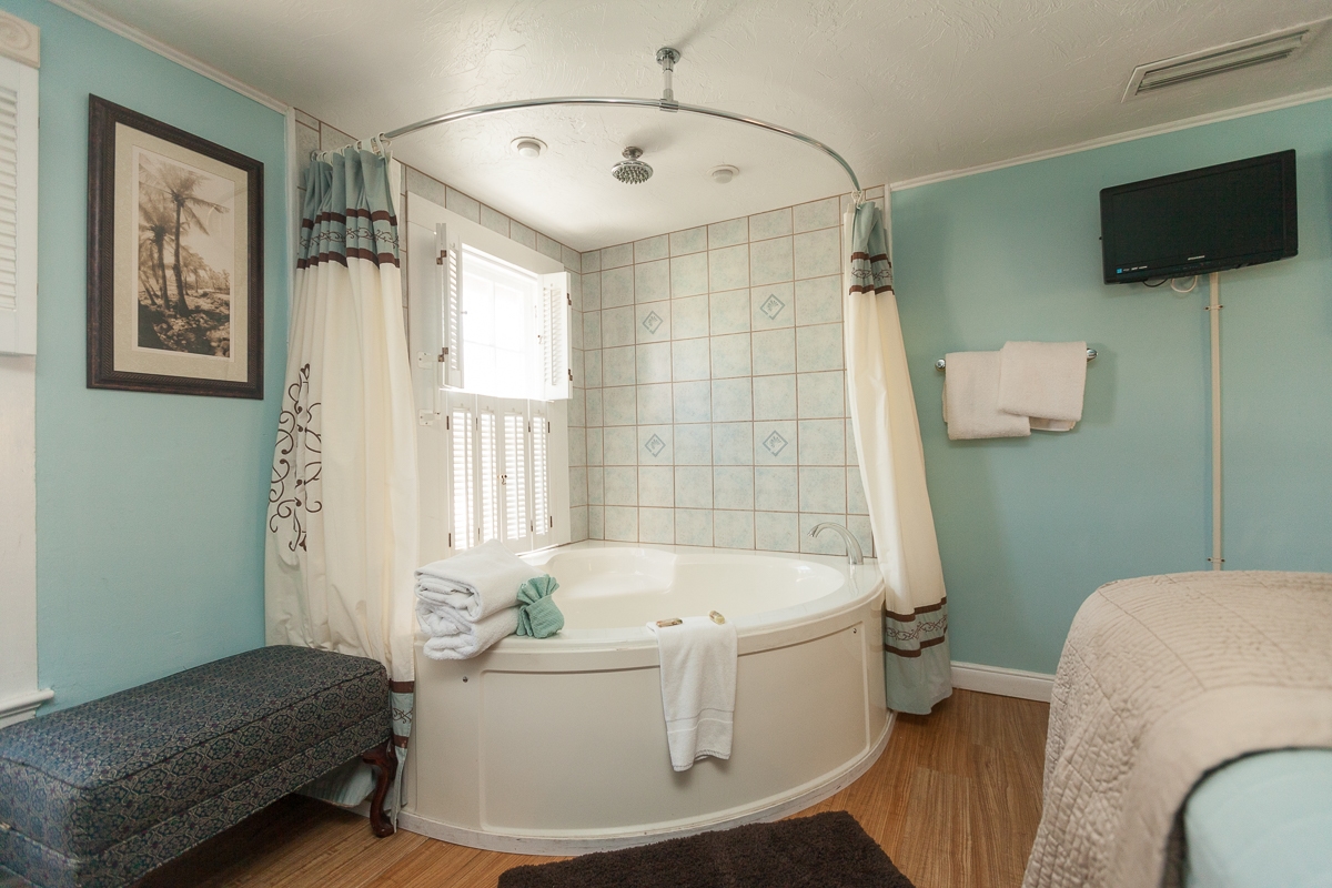 Two-person whirlpool tub in corner of bedroom with upholstered bench next to it.