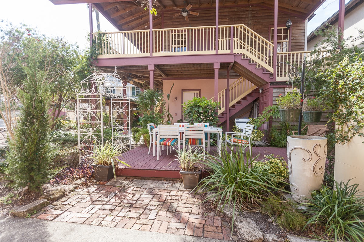 Exterior brick courtyard with raised patio seating area surrounded by foliage and inn with outdoor steps leading to balcony in background.