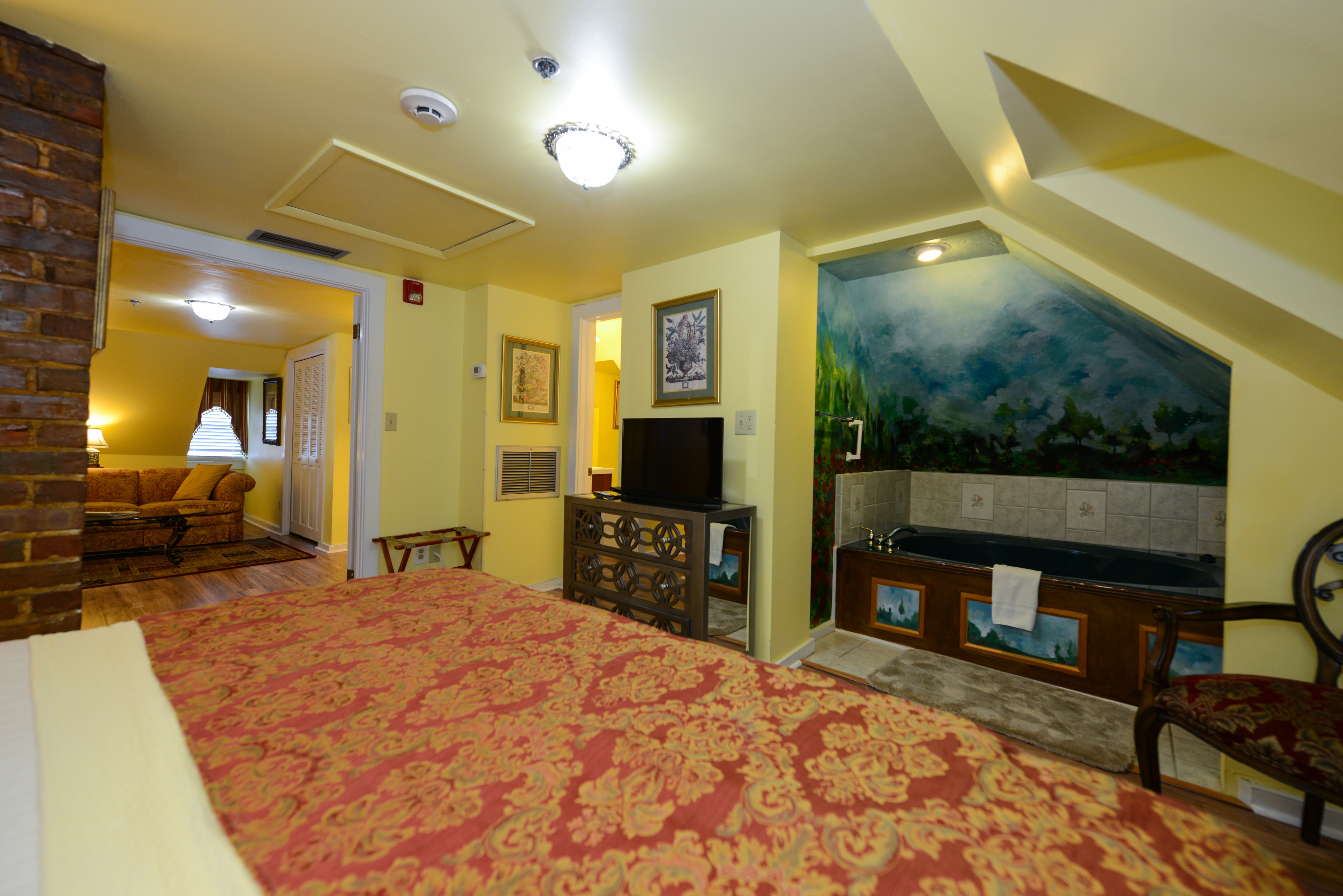 Third-floor bedroom shows the foot of the king bed draped in an elegant red and gold bedspread.  Opposite the bed is a lighted recessed nook with a two-person whirlpool tub.