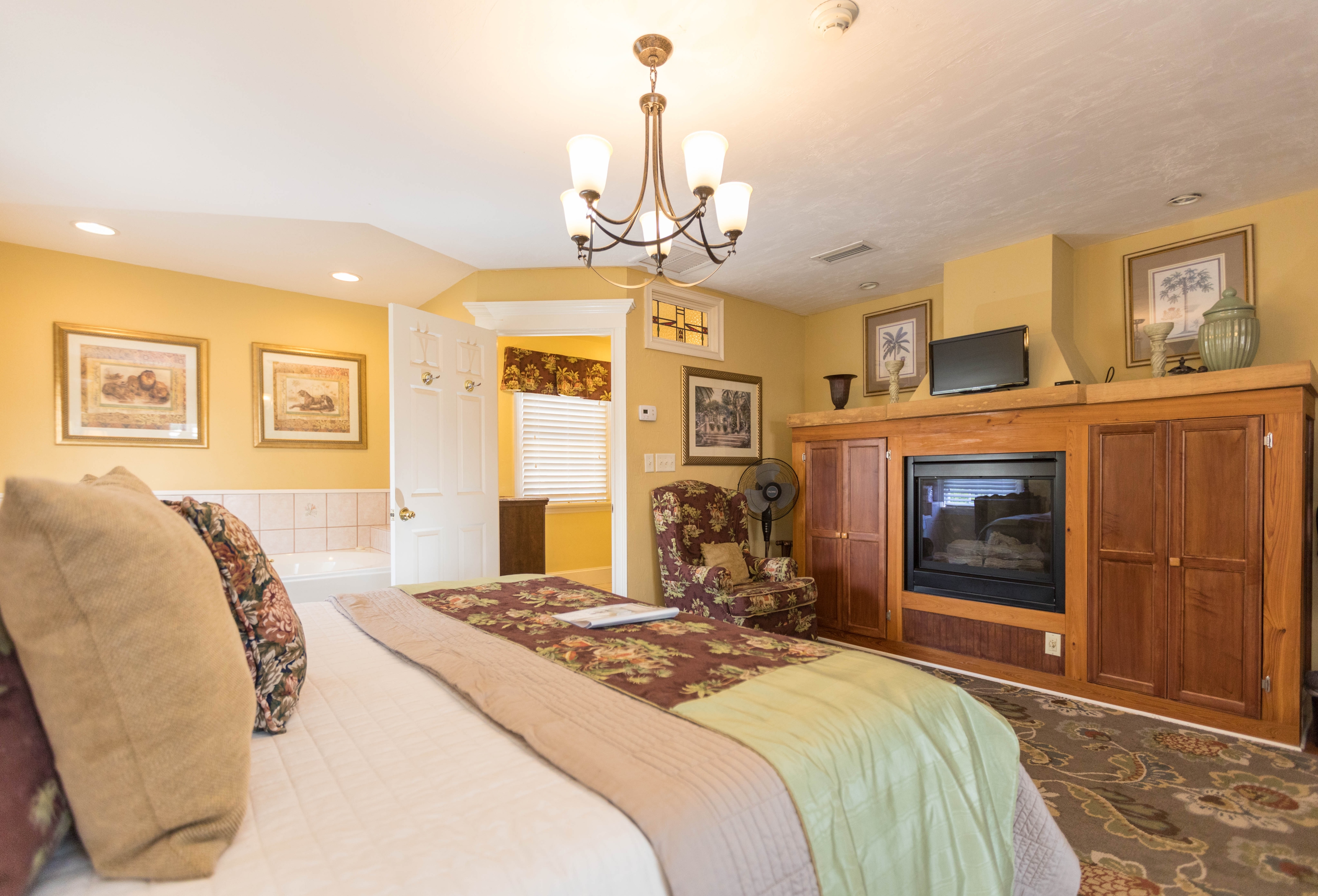 Bright, sunny bedroom with king bed opposite a fireplace flanked with wooden cabinets