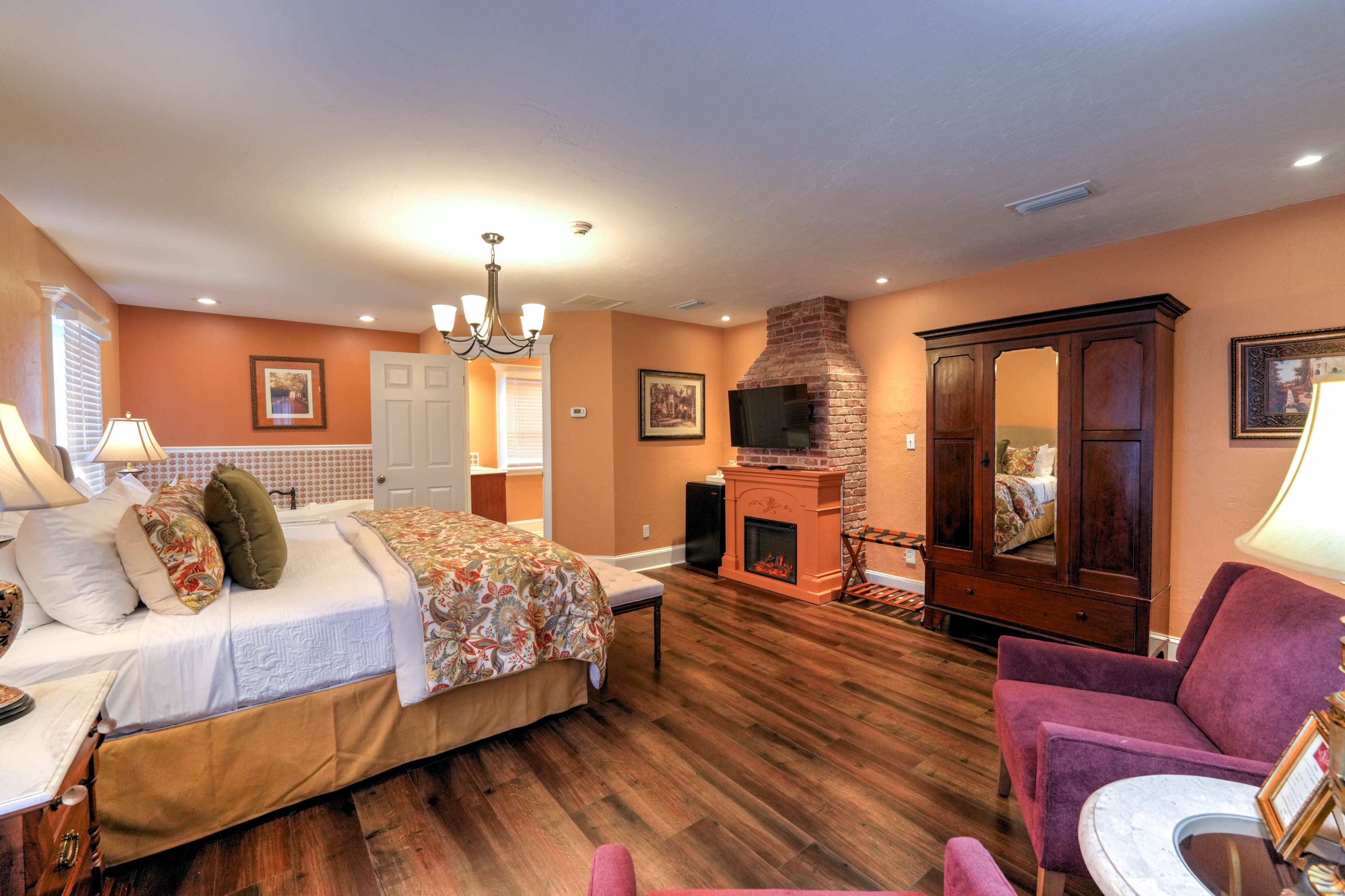 Bright, sunny bedroom with king bed opposite a fireplace flanked with wooden cabinets