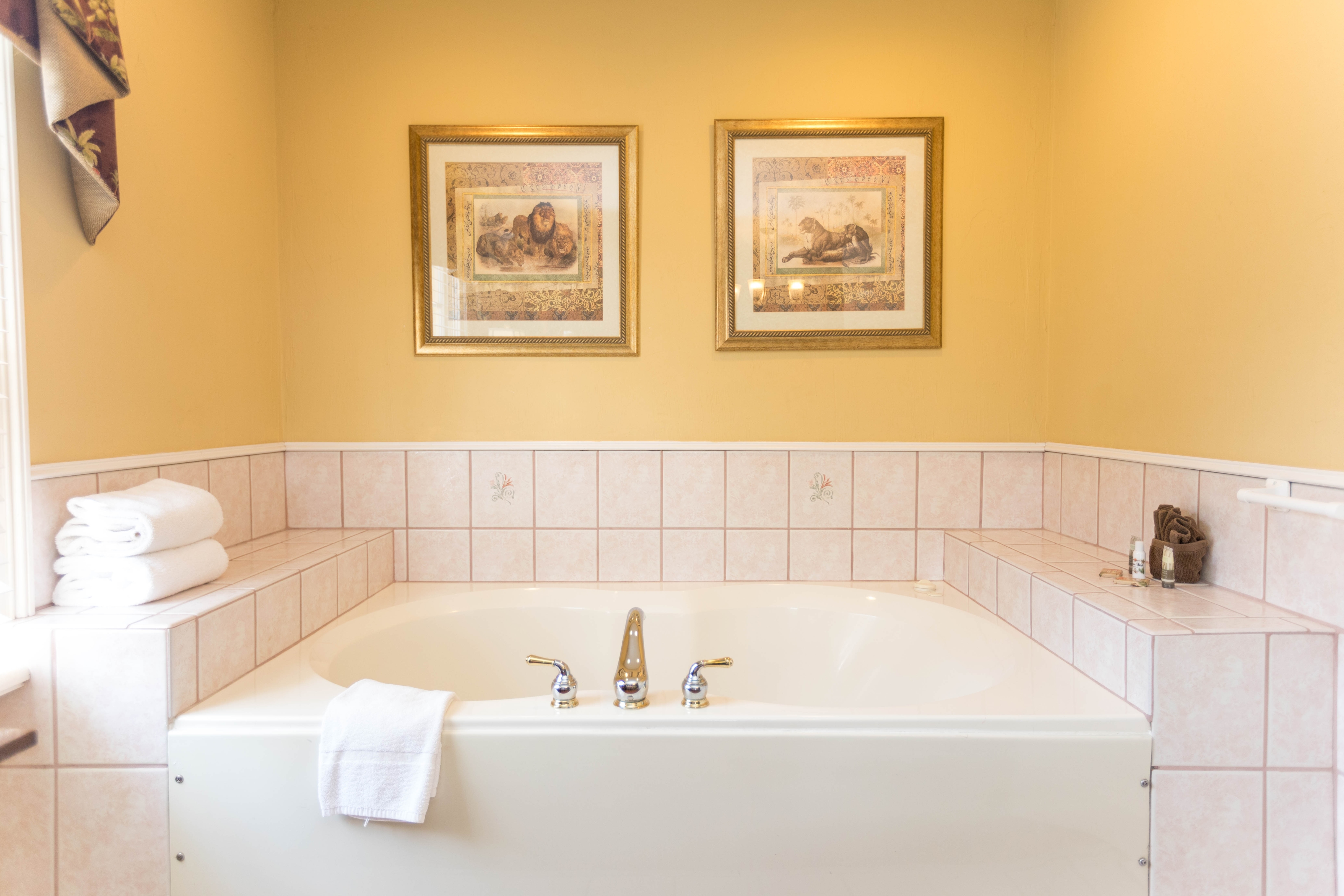 Gleaming white whirlpool tub has white tiled surround with plush white towels folded and ready nearby.