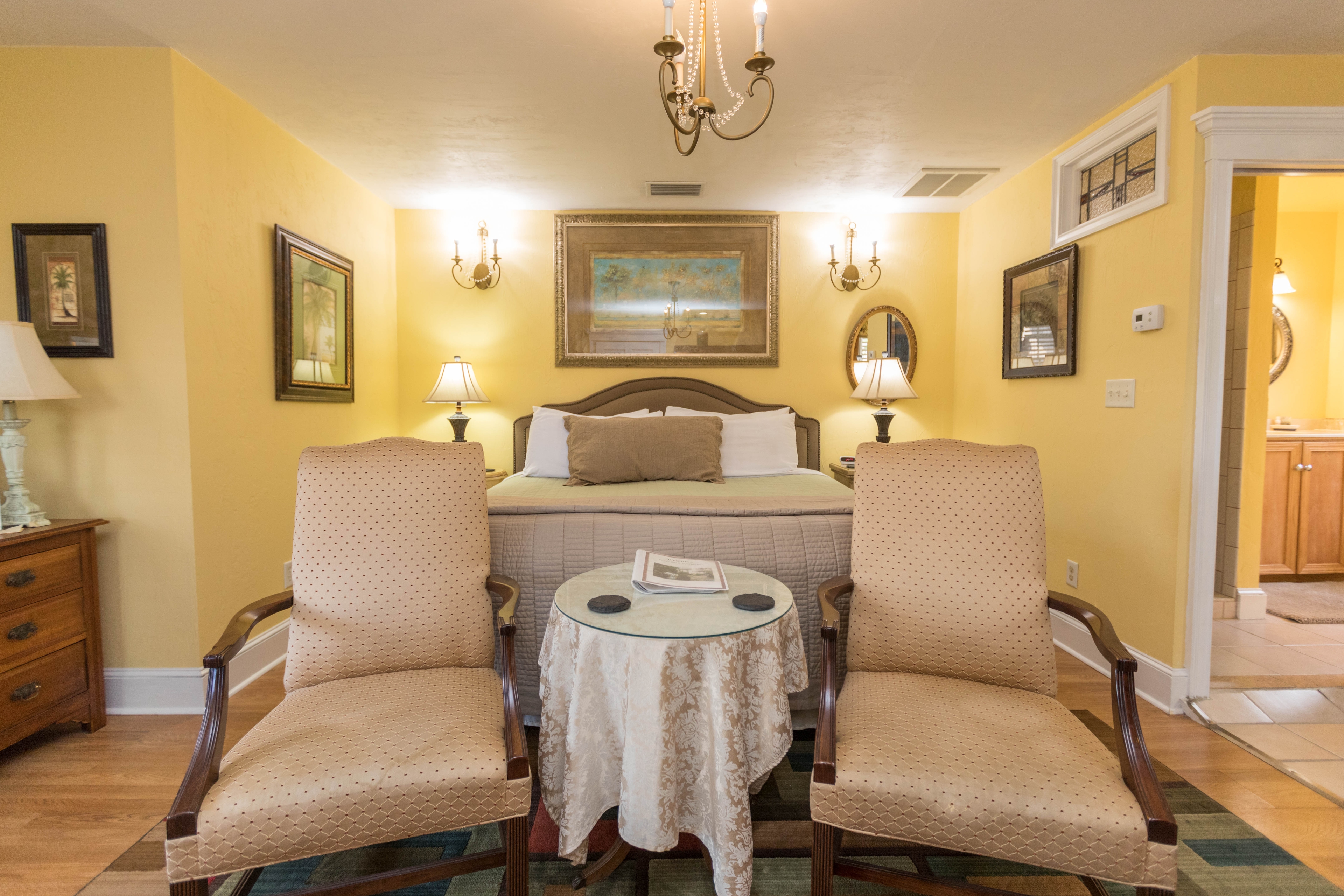 The sitting area at the foot of the bed features two upholstered ivory chairs with a round occasional table between them.