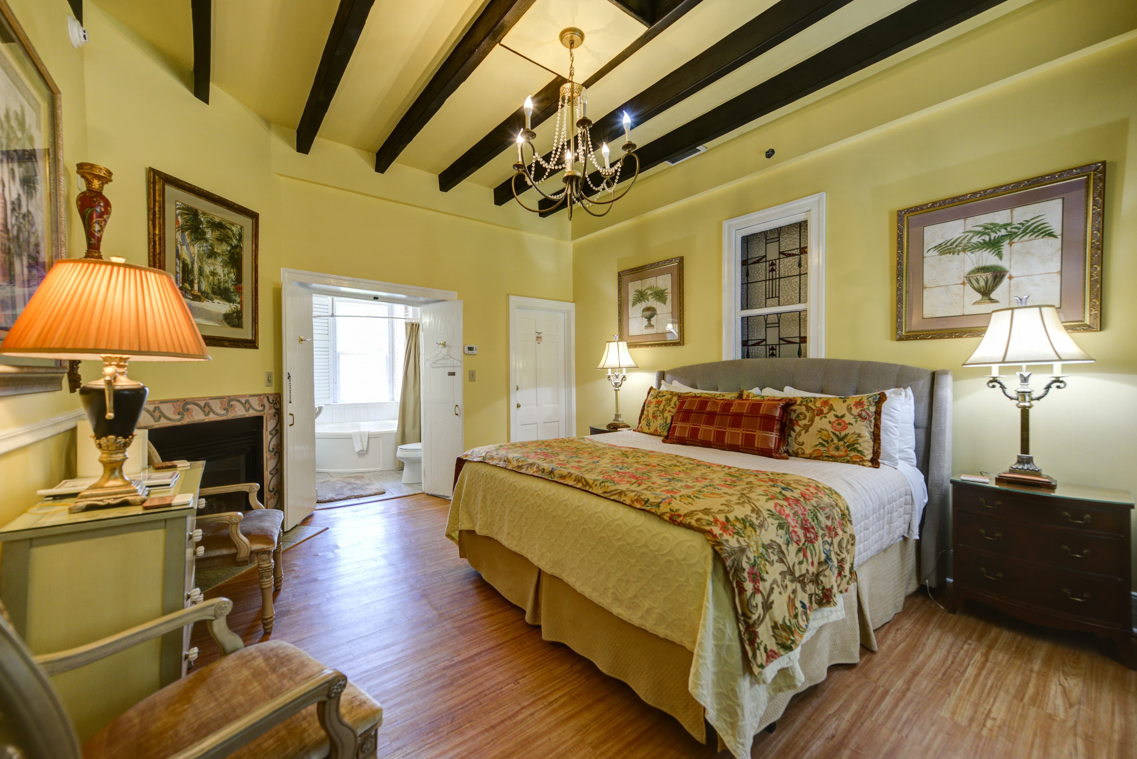 Warm and inviting bedroom with beam ceiling and richly decorated with a king bed, antique furniture and lovely artwork