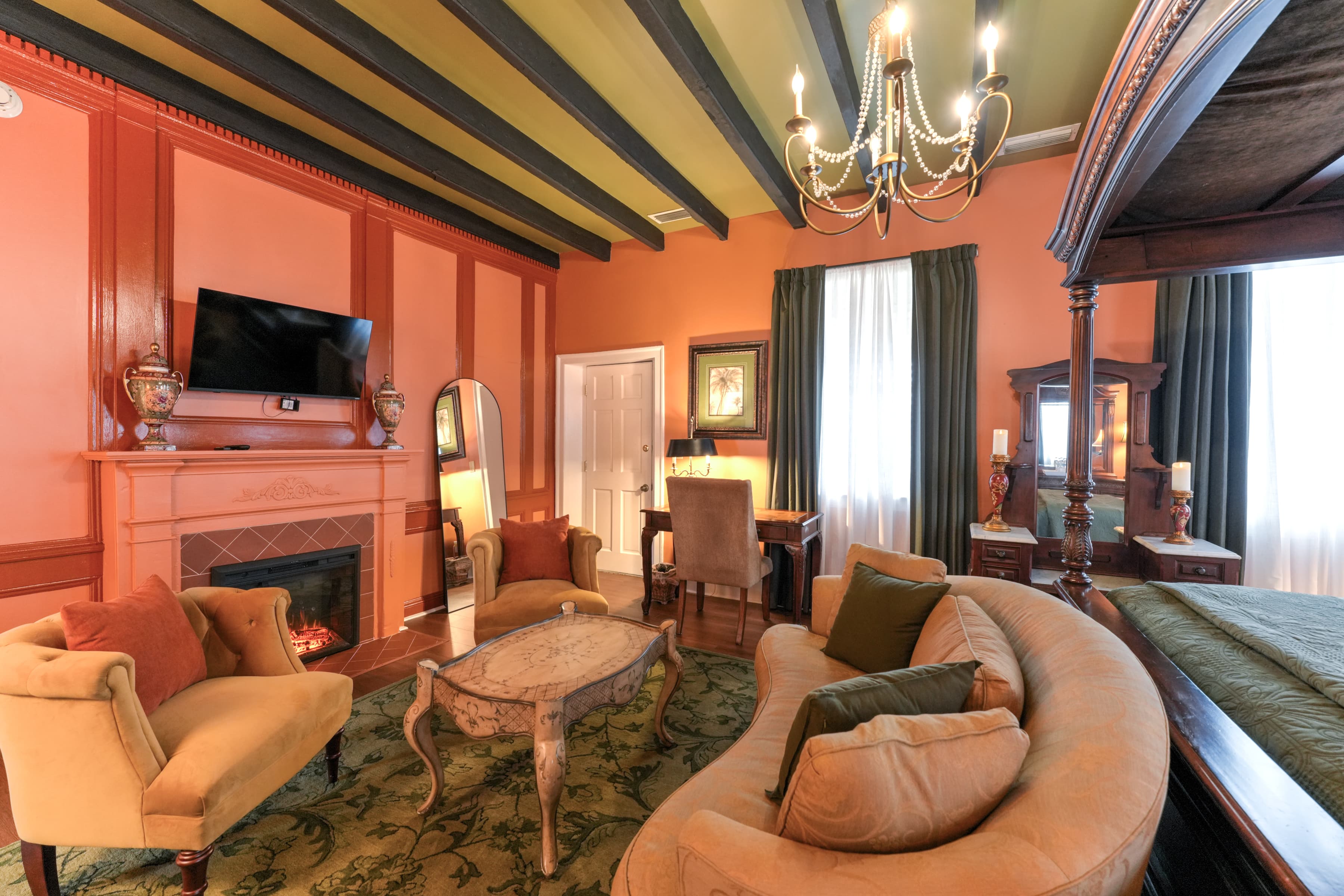 Loveseat at foot of bed, large windows with color themed drapes, and writing desk with chair, sitting area with oriental area rug and upholstered loveseat and armchairs