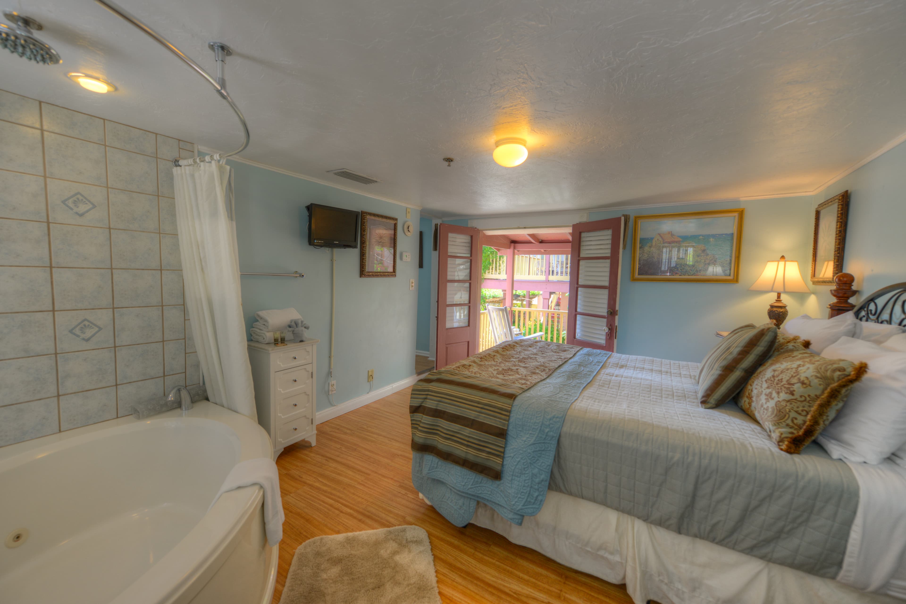 Tranquil bedroom with two-person whirlpool tub, queen bed, and French doors at far end of room leading to private balcony.