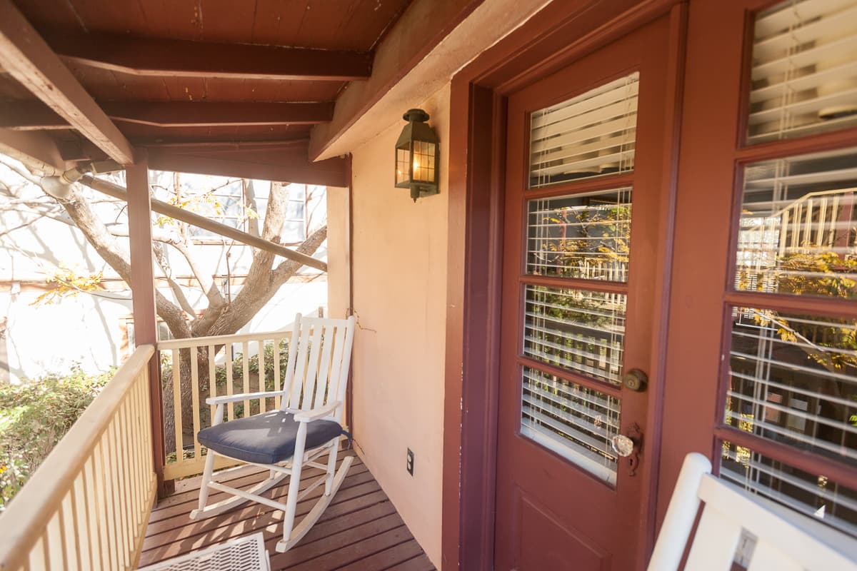 Private outdoor balcony with rocking chairs and French doors leading to bedroom.