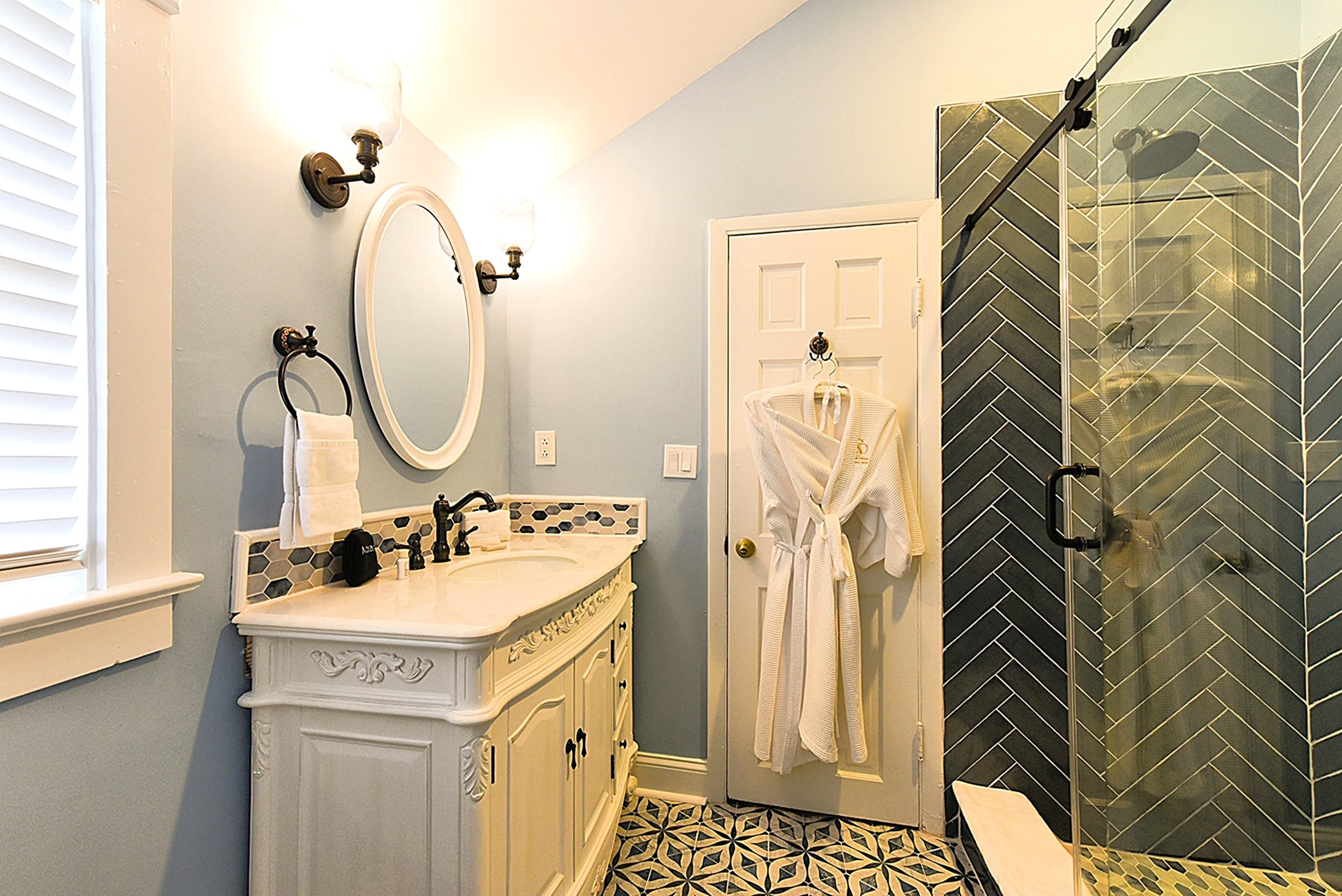 Bathroom with light blue walls, white toilet, window with blinds & striped valance, hairdryer in vanity cabinet and sink with vanity.