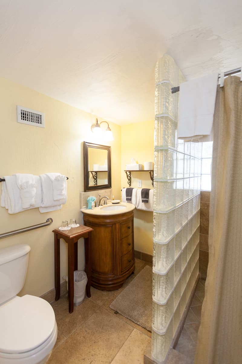 Private bathroom in light neutral earthtones with toilet, sink with cabinet, and walk-in shower.