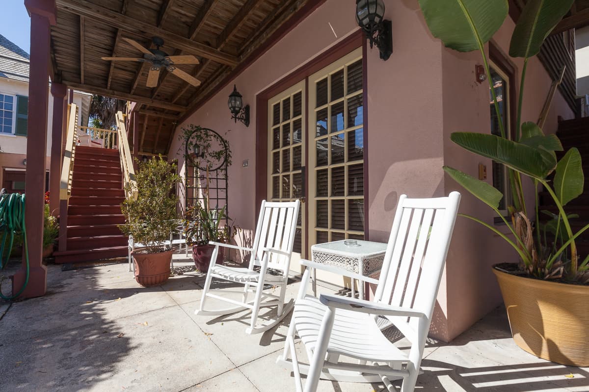 Seating area outside with white chairs near French doors, large potted plants