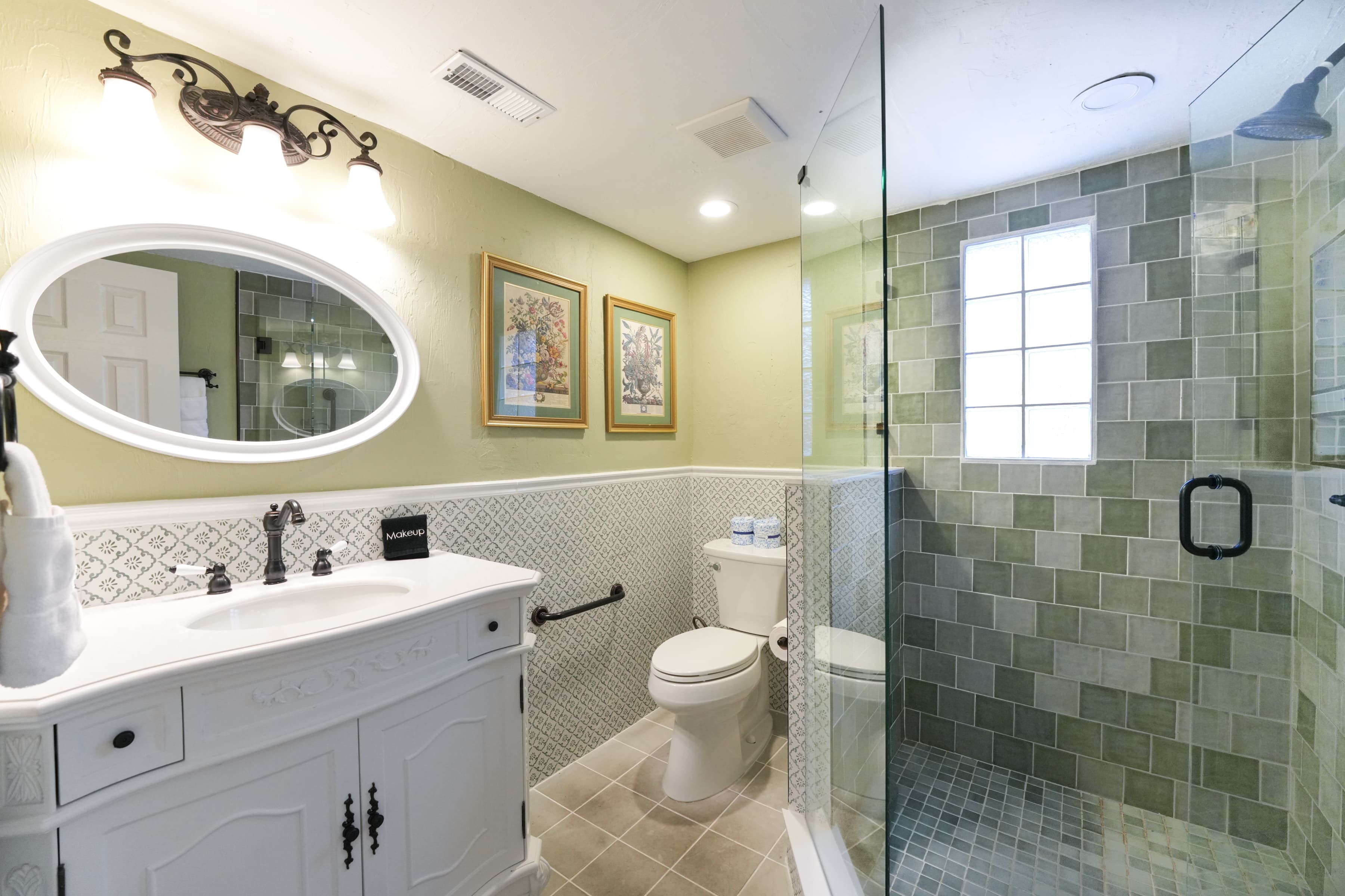 Private bathroom in light green color theme with antique white vanity, walk-in shower. and toilet