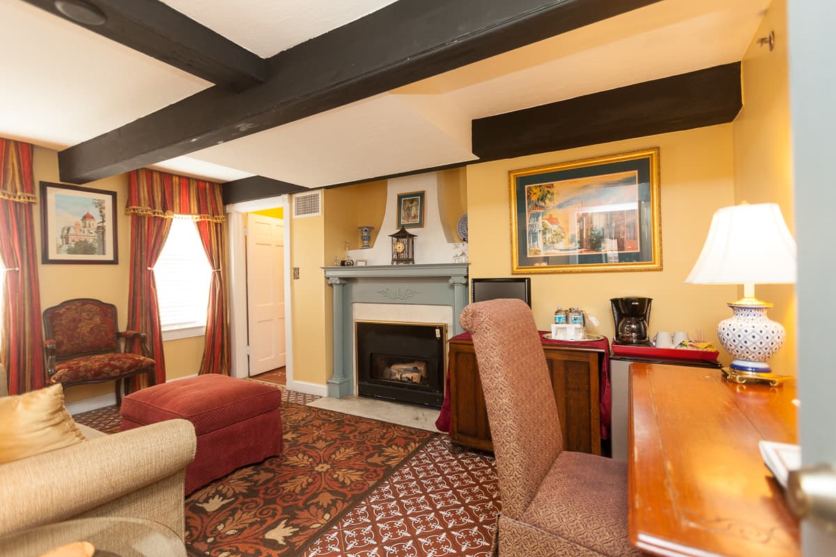 Sitting area with writing desk and chair, sofa, ottoman, and fireplace with painted wood mantel.