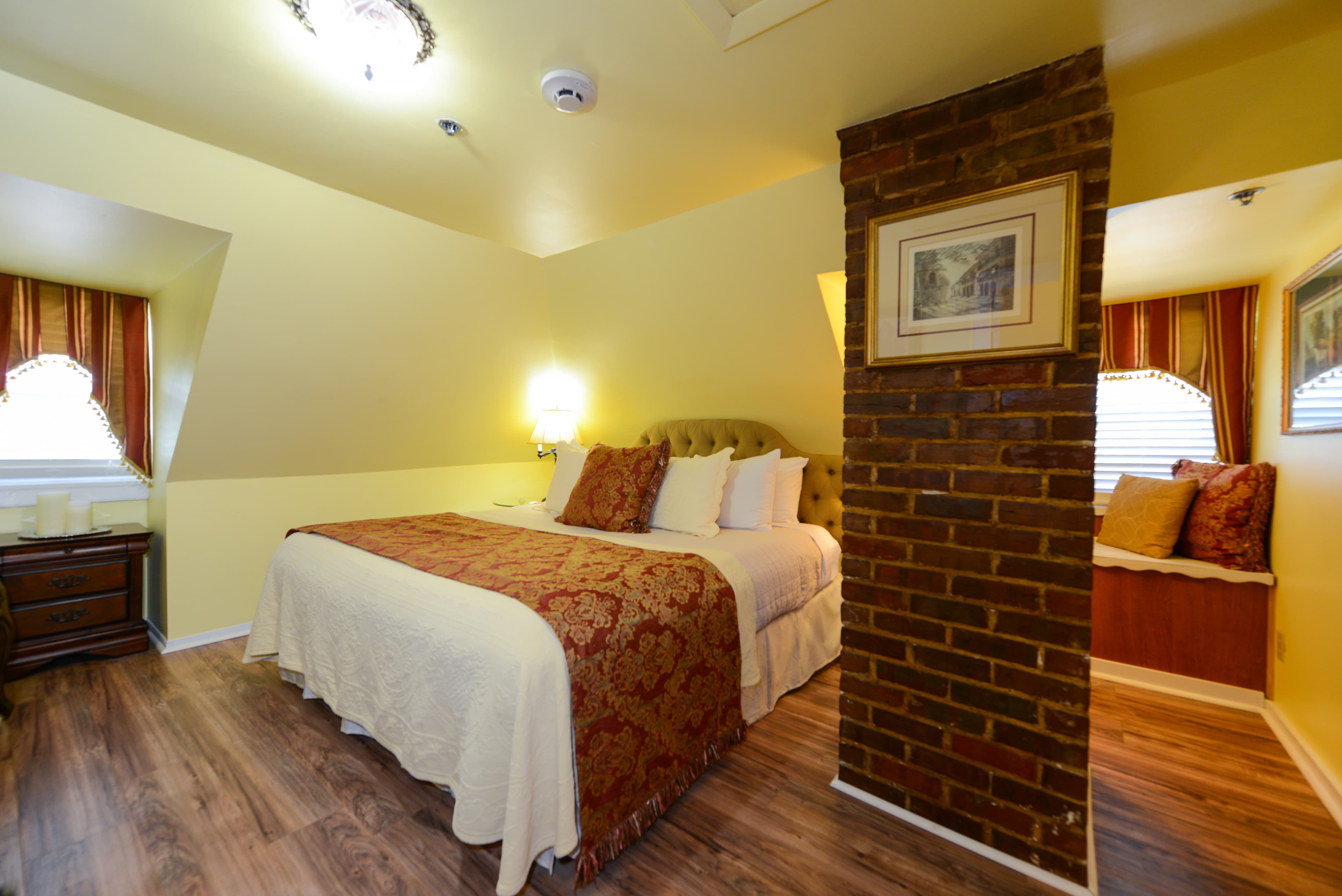 A warm and welcoming third floor bedroom with cheerful yellow walls, finished wood floors, a king bed, and a window seat with plump pillows.