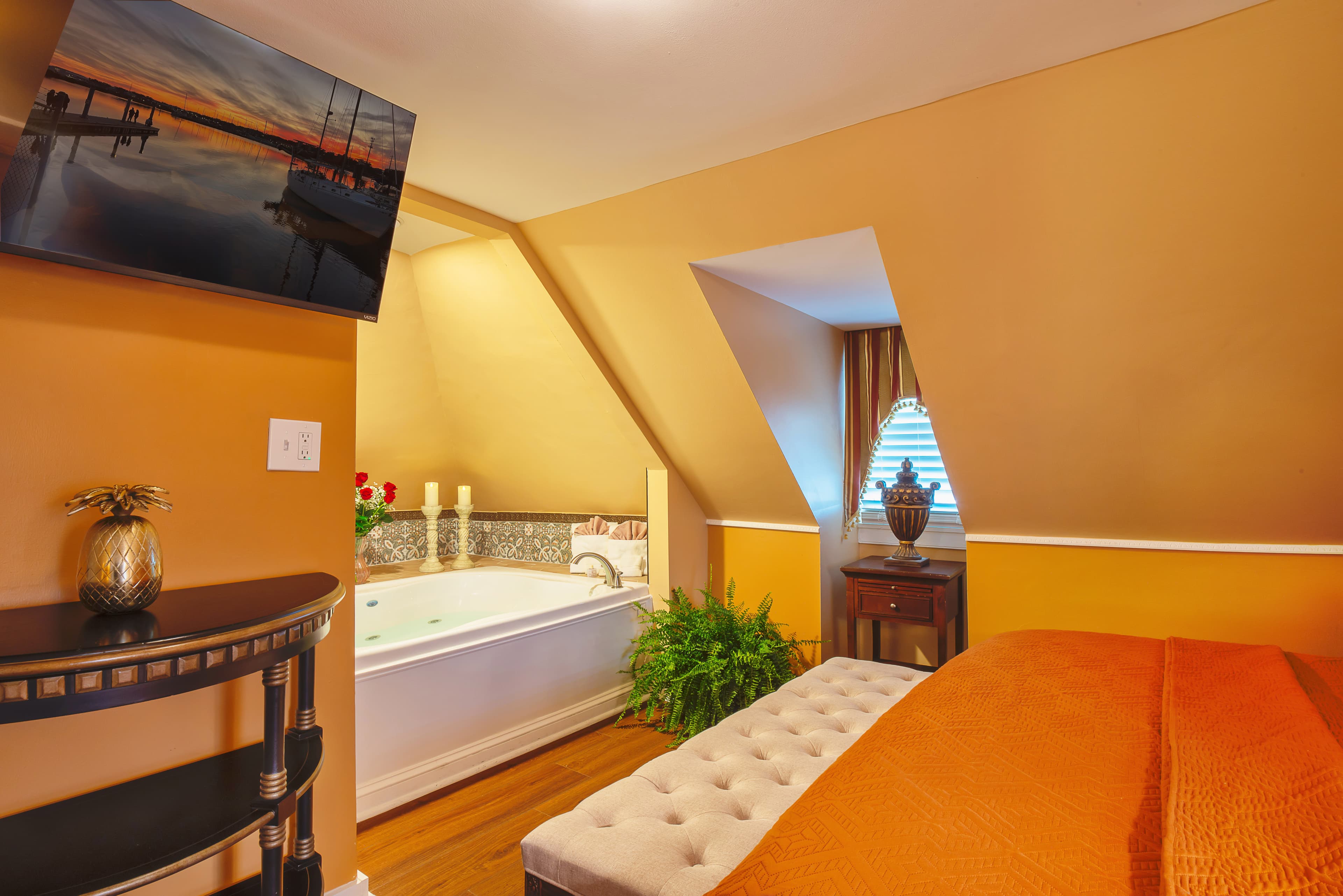 Third-floor bedroom with yellow walls, white trim, and finished wood floors.  The king-size bed with decorative pillows. The ceiling slopes down just above the headboard.