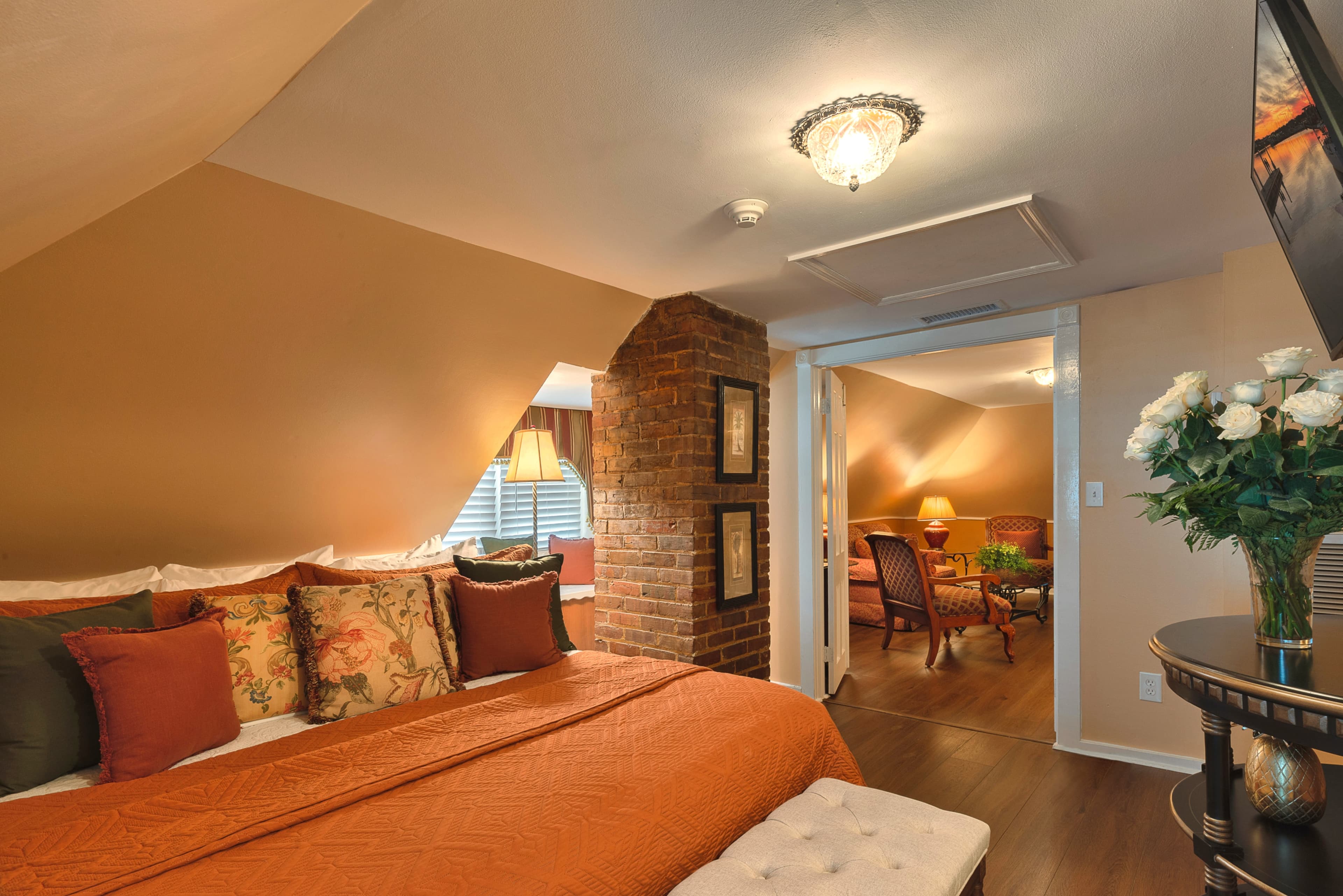 Cozy third-floor bedroom opposite the king bed is a bureau with a flat-screen TV.  To the left of the TV is the bathroom doorway, and recessed in a nook to the right is a whirlpool tub for two.