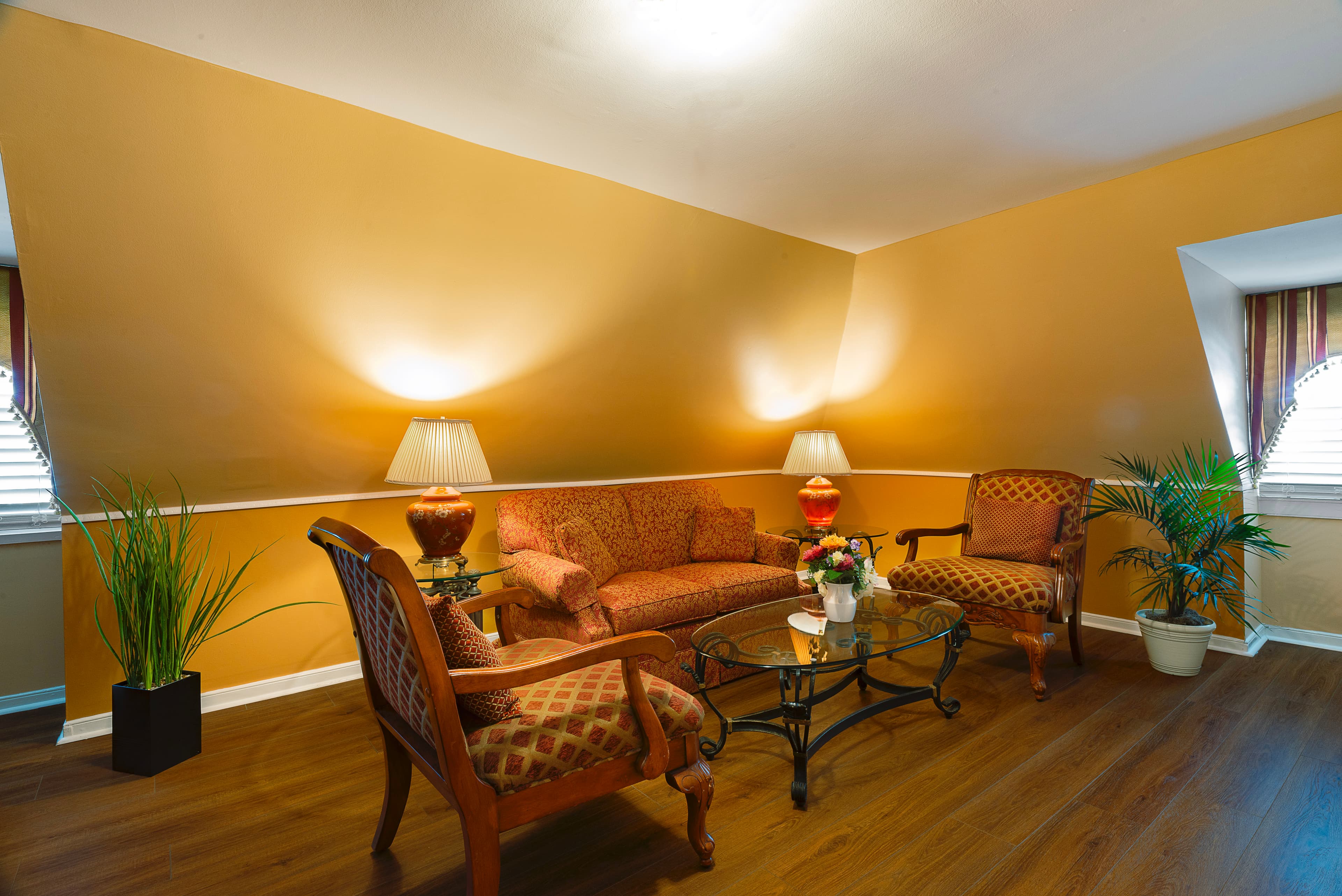 French doors stand open to the bedroom from an inviting sitting room with cheering walls and white trim, finished wood floors, sloped ceilings on one side, and lovely antique furniture.