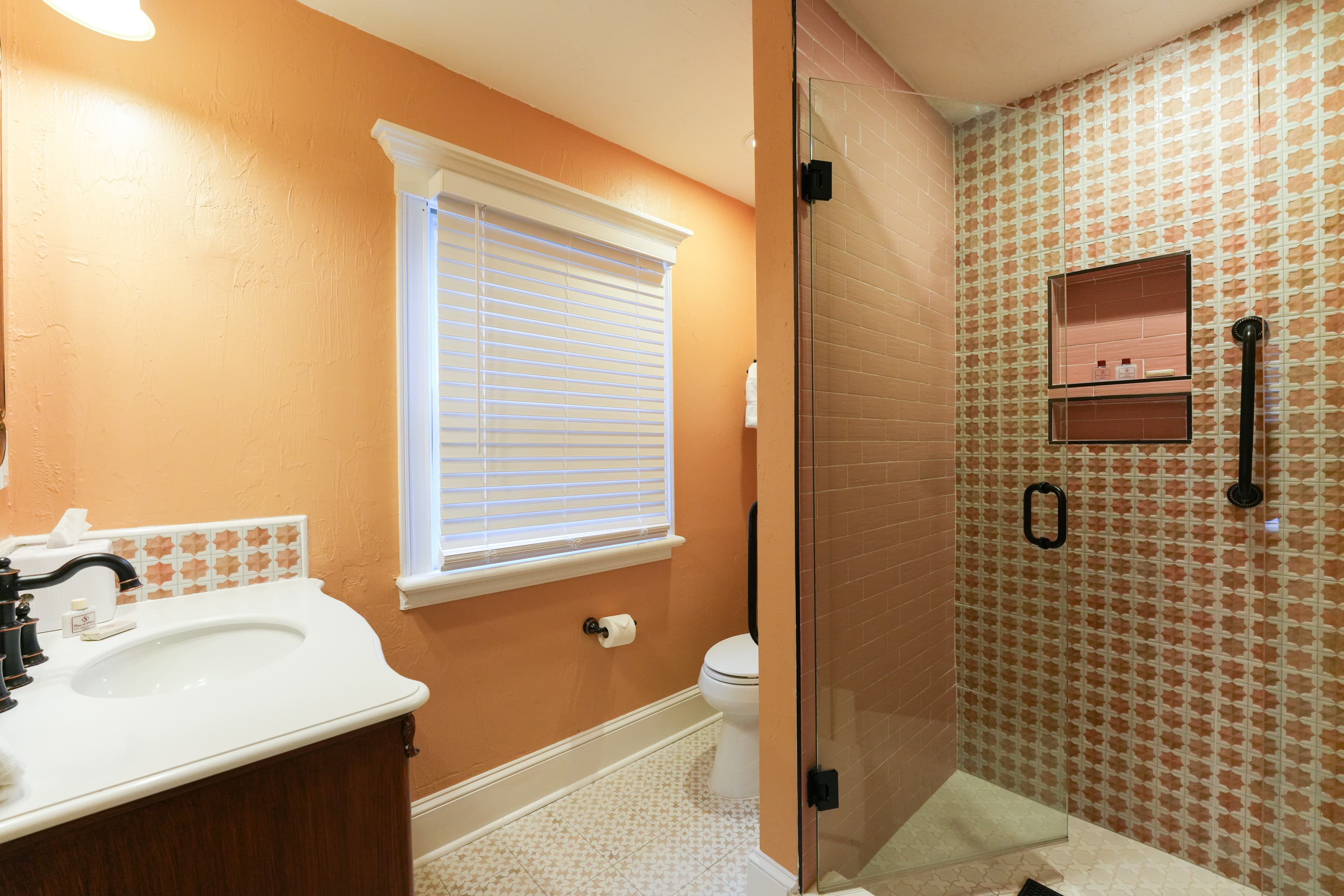 Bright, clean bathroom with walk-in shower, toilet, sink with vanity, and window with blinds