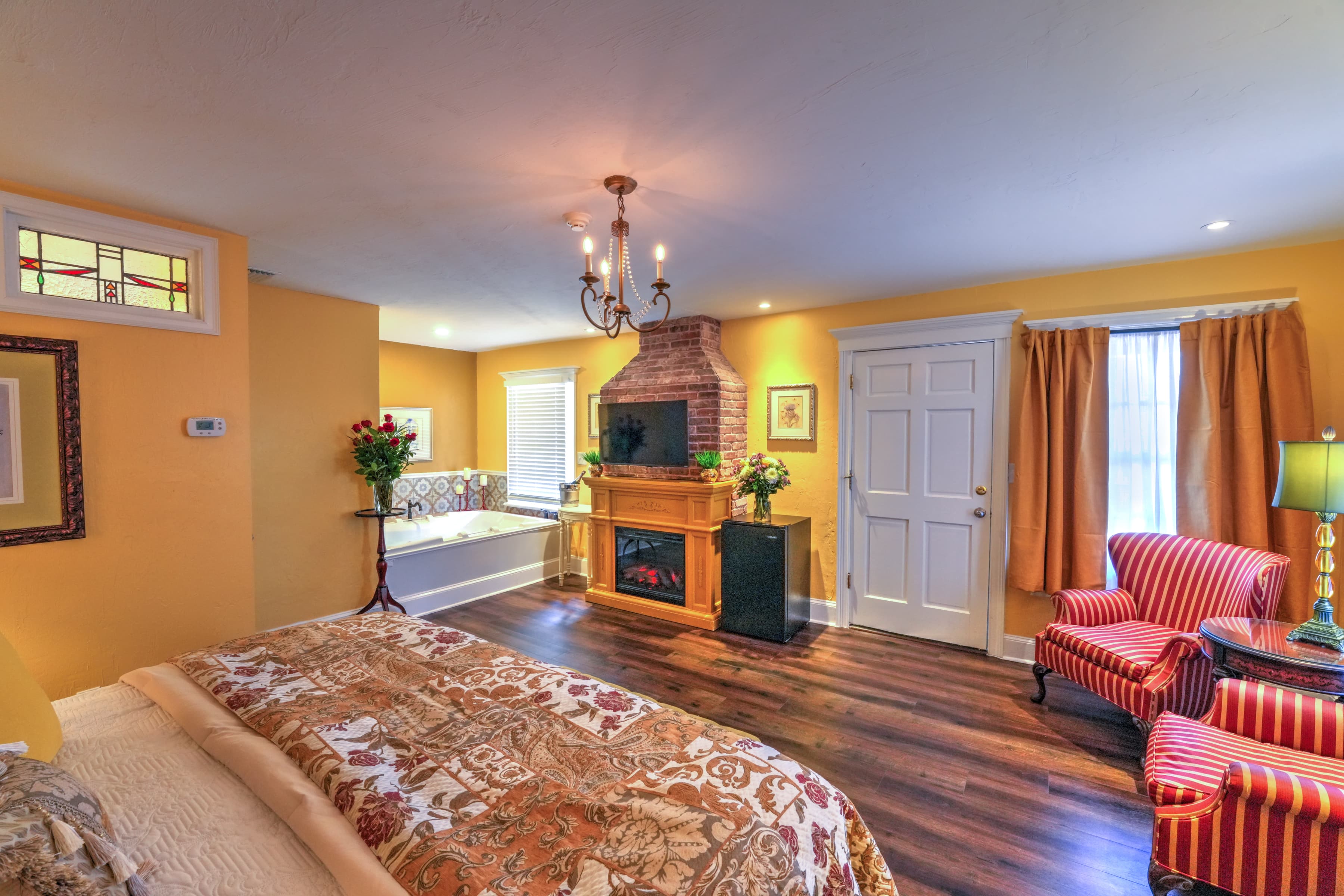 An eclectically decorated room with king bed, two spacious and comfortable upholstered chairs, finished wood floors, electric fireplace