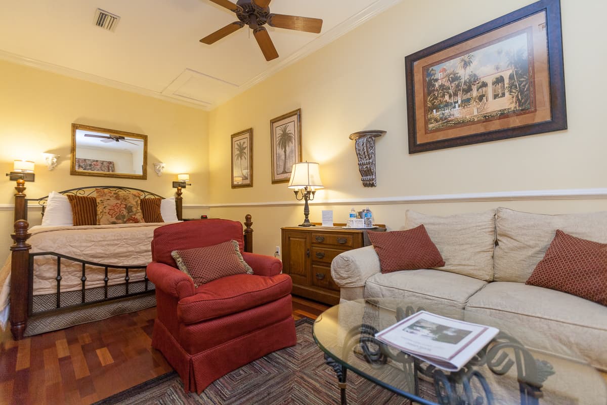 Welcoming guestroom in warm reds and earthtones with a California king bed and a sitting area with armchair, sofa, and coffee table.