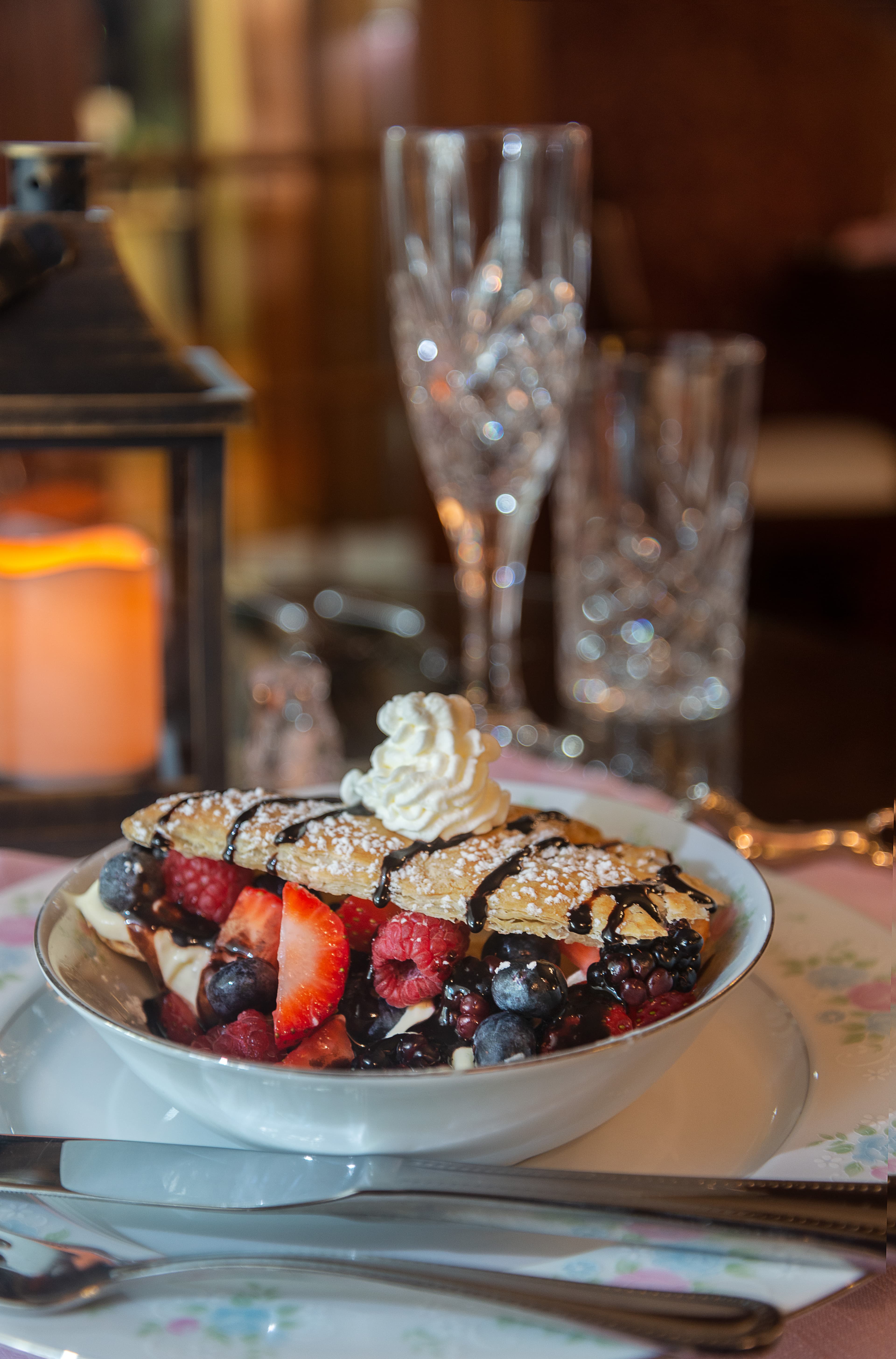 A bowl of mixed berries topped with whipped cream and a chocolate-drizzled pastry shell.