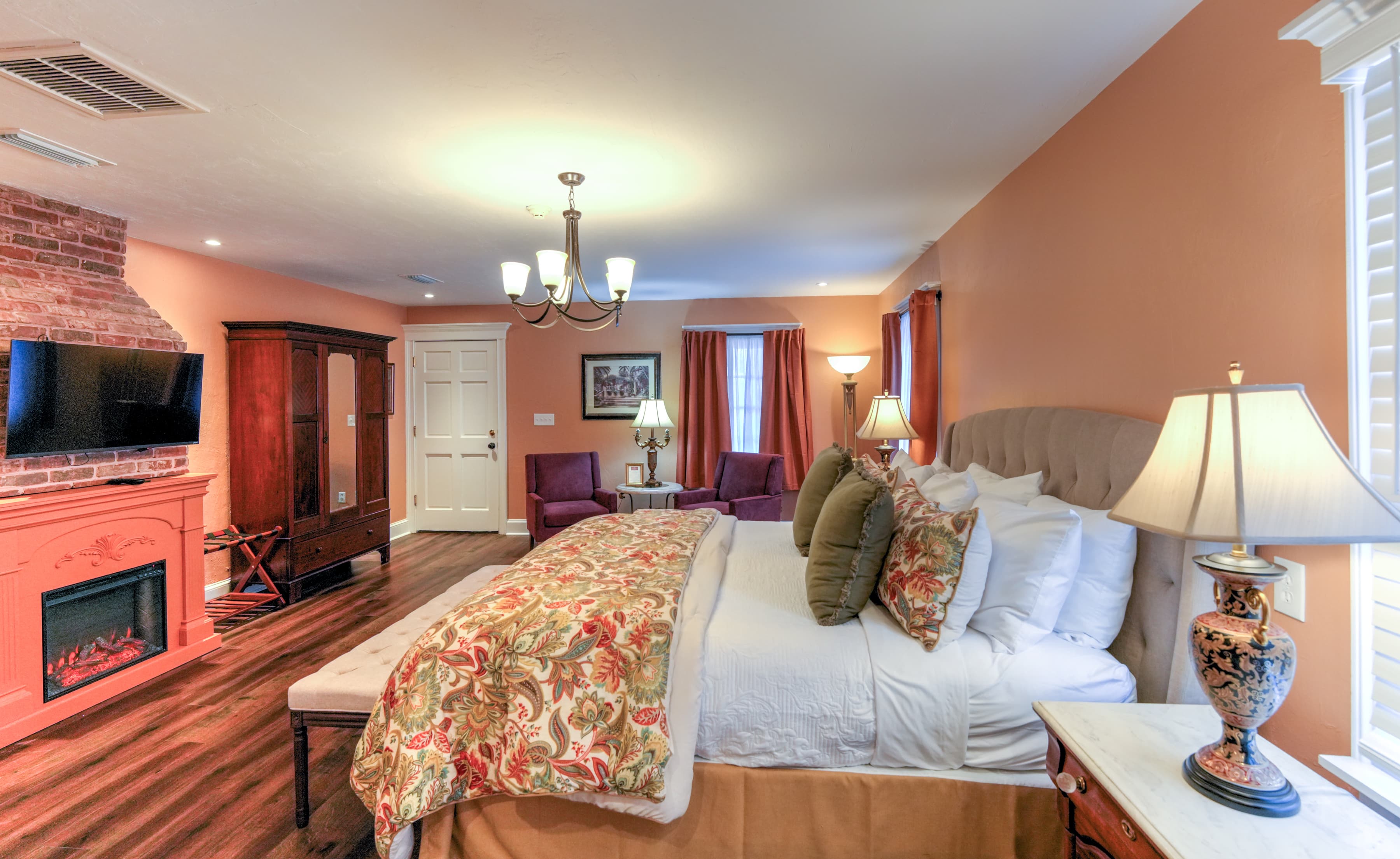 A cozy bedroom featuring a large bed, armchairs, and a brick accent wall.