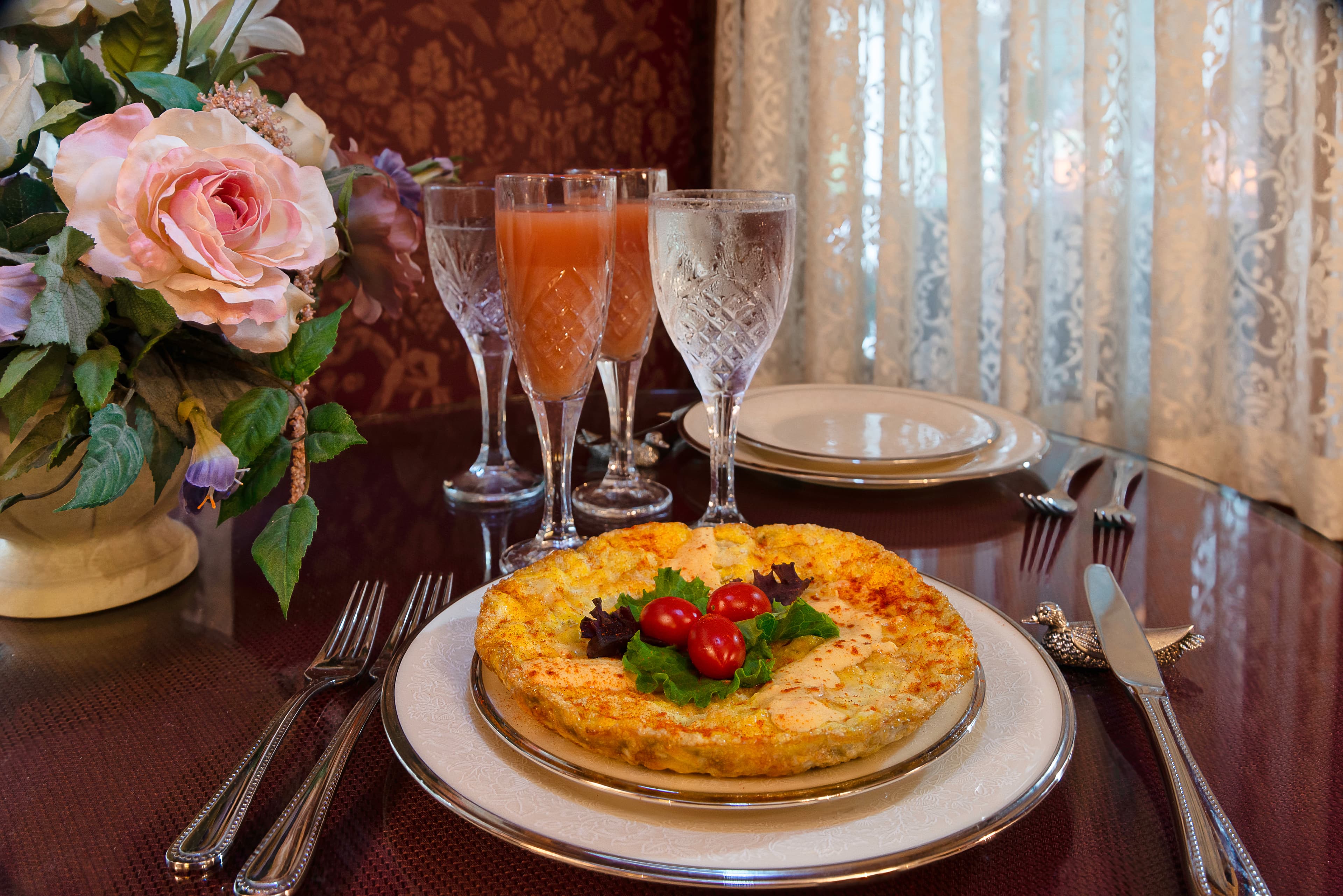 A beautifully arranged table featuring a vegetable frittata, elegant glassware, and a floral centerpiece.