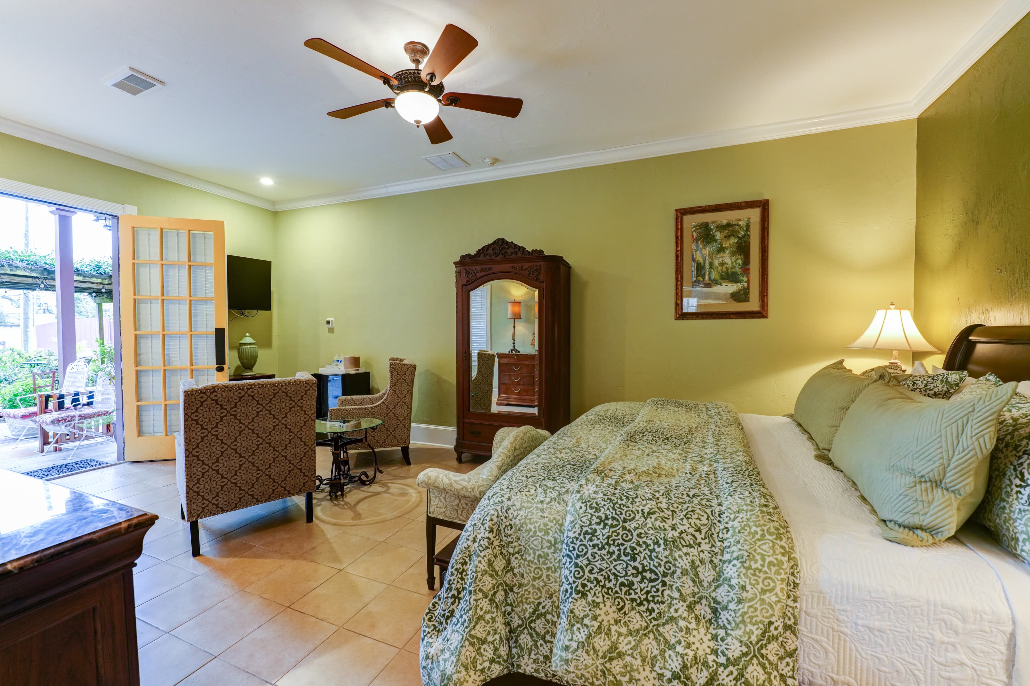 Spacious guestroom with king bed and antique armoire. On the other side of the room is a comfortable seating area with two comfortable chairs and flat-screen TV for entertainment.