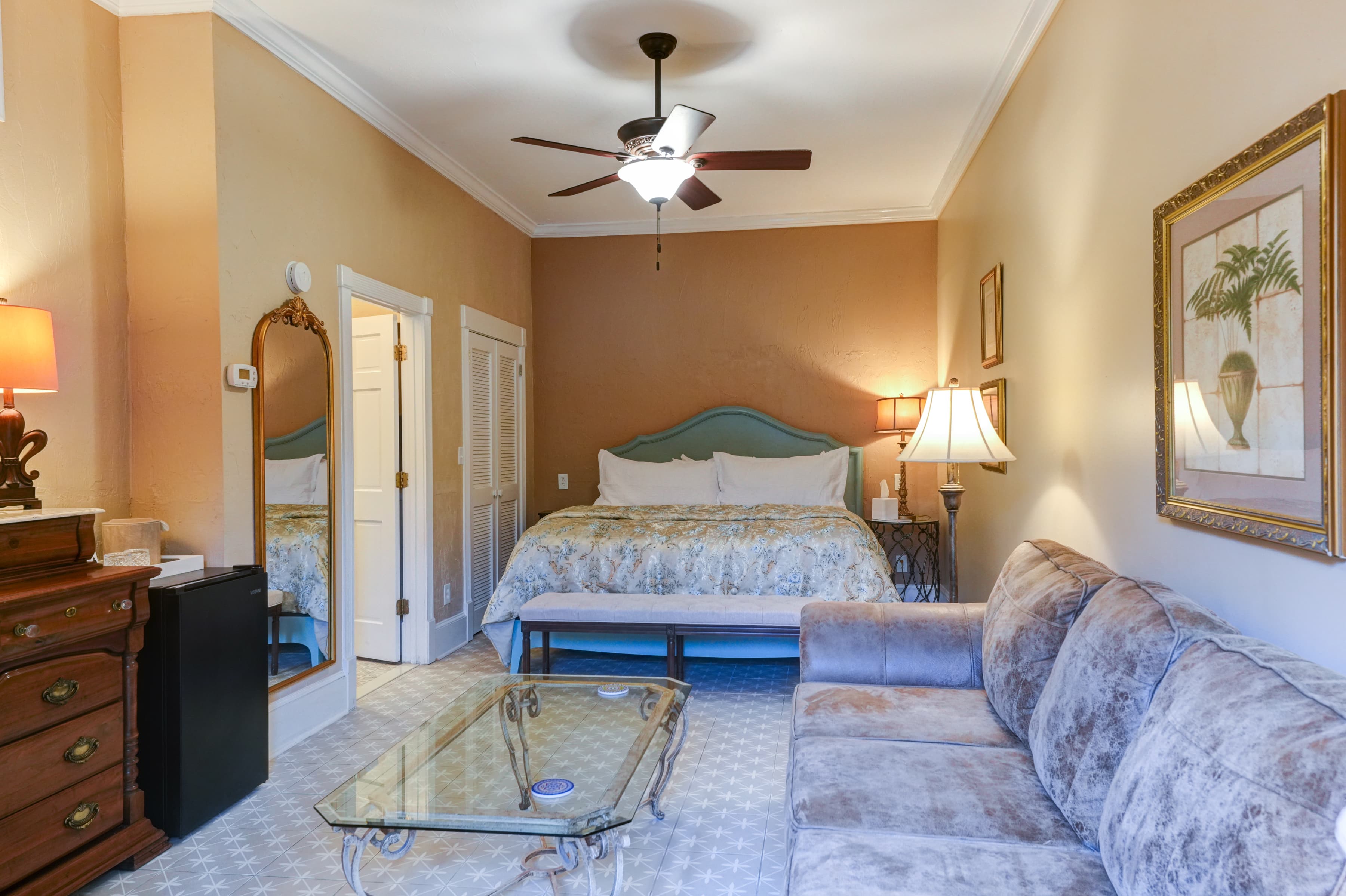 A cozy bedroom featuring a queen bed, soft couch, and a glass coffee table.