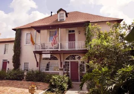 Historic building with a balcony, flags, and surrounding greenery.