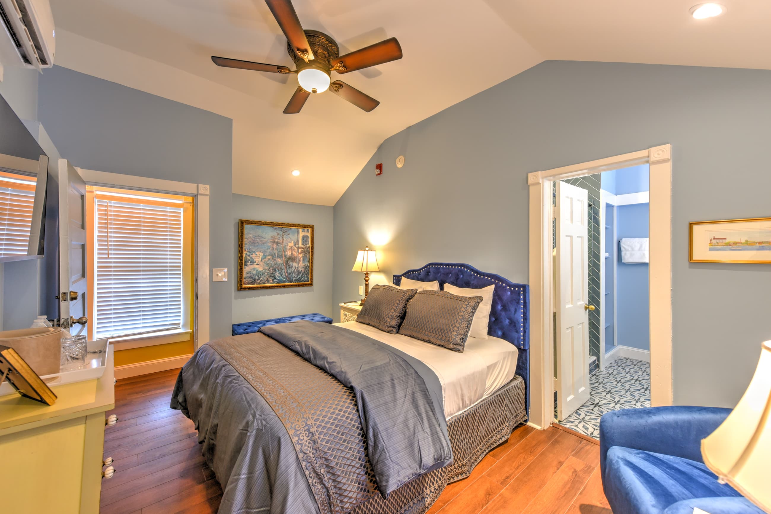 A cozy bedroom with a blue accent wall, a comfortable bed, and natural light streaming through the window.