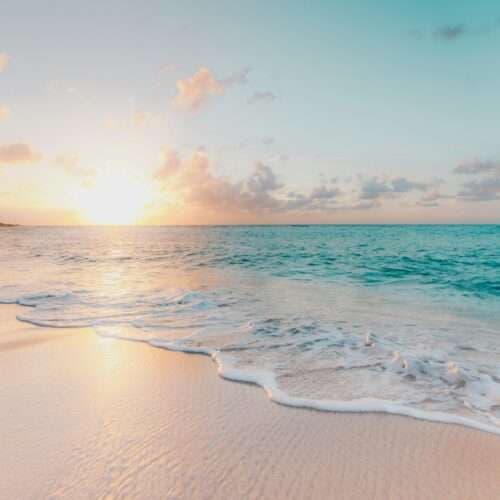 A tranquil beach scene at sunrise with gentle waves lapping the shore.