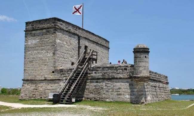 A historic stone fort with a flag, surrounded by grassy land and clear blue skies.