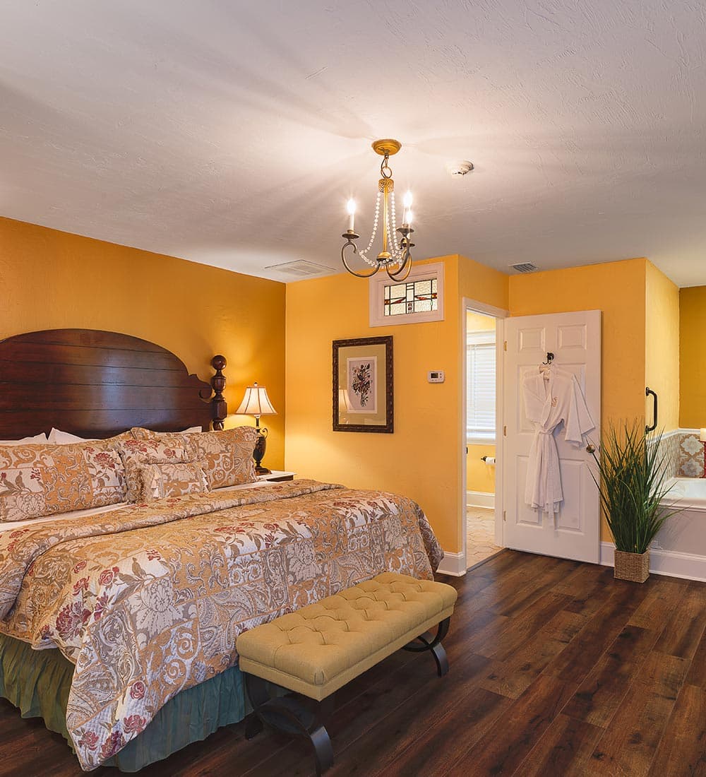 A cozy bedroom featuring a yellow wall, patterned bedding, a chandelier, and an adjoining bathroom.