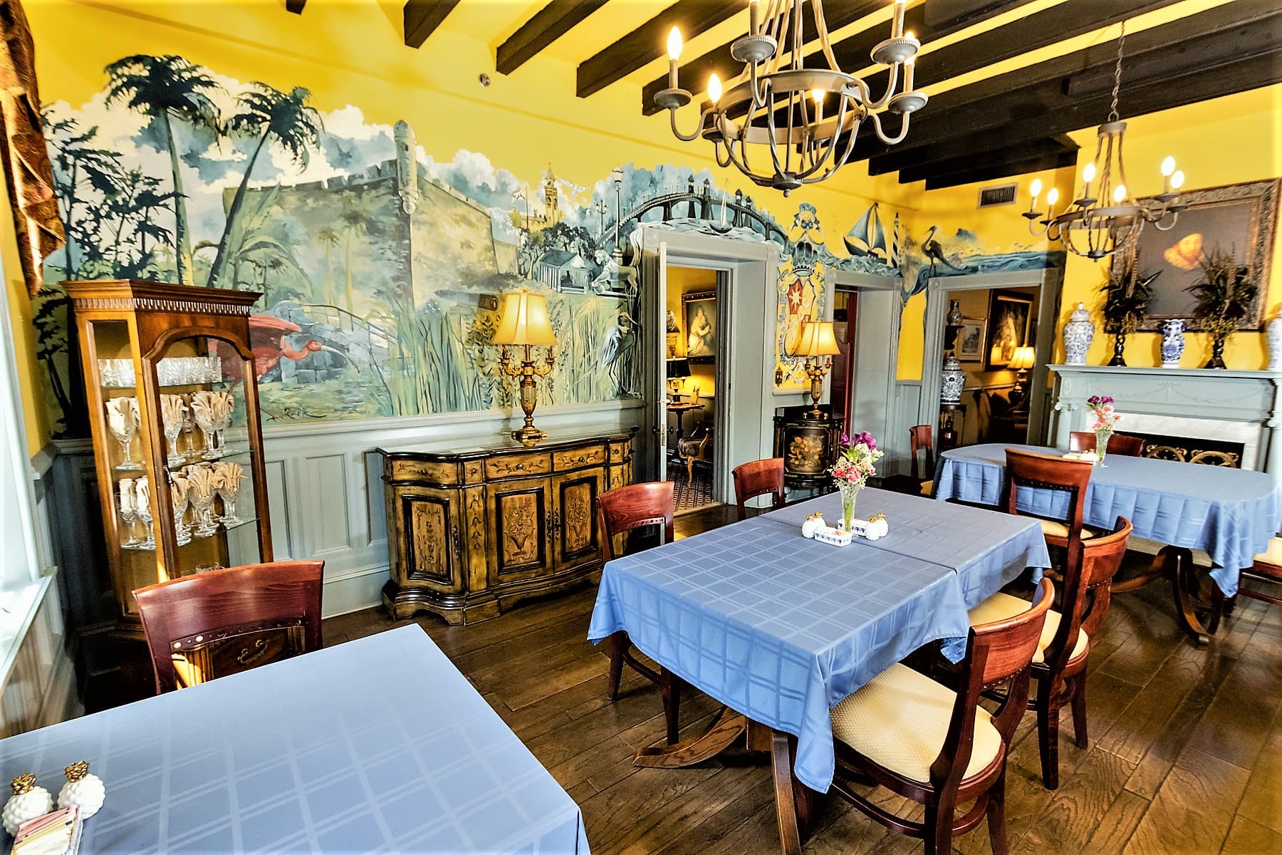 A brightly decorated dining room featuring blue tables, wooden accents, and a vibrant mural.