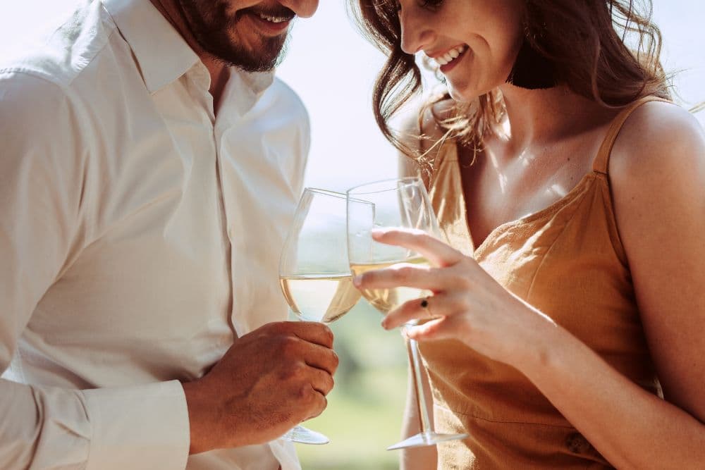 A couple joyfully clinks wine glasses together, smiling at each other.
