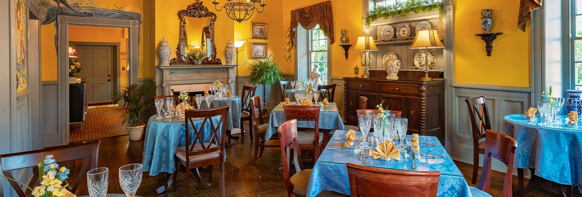 Cozy restaurant interior featuring elegantly set tables with blue linens and warm yellow walls.