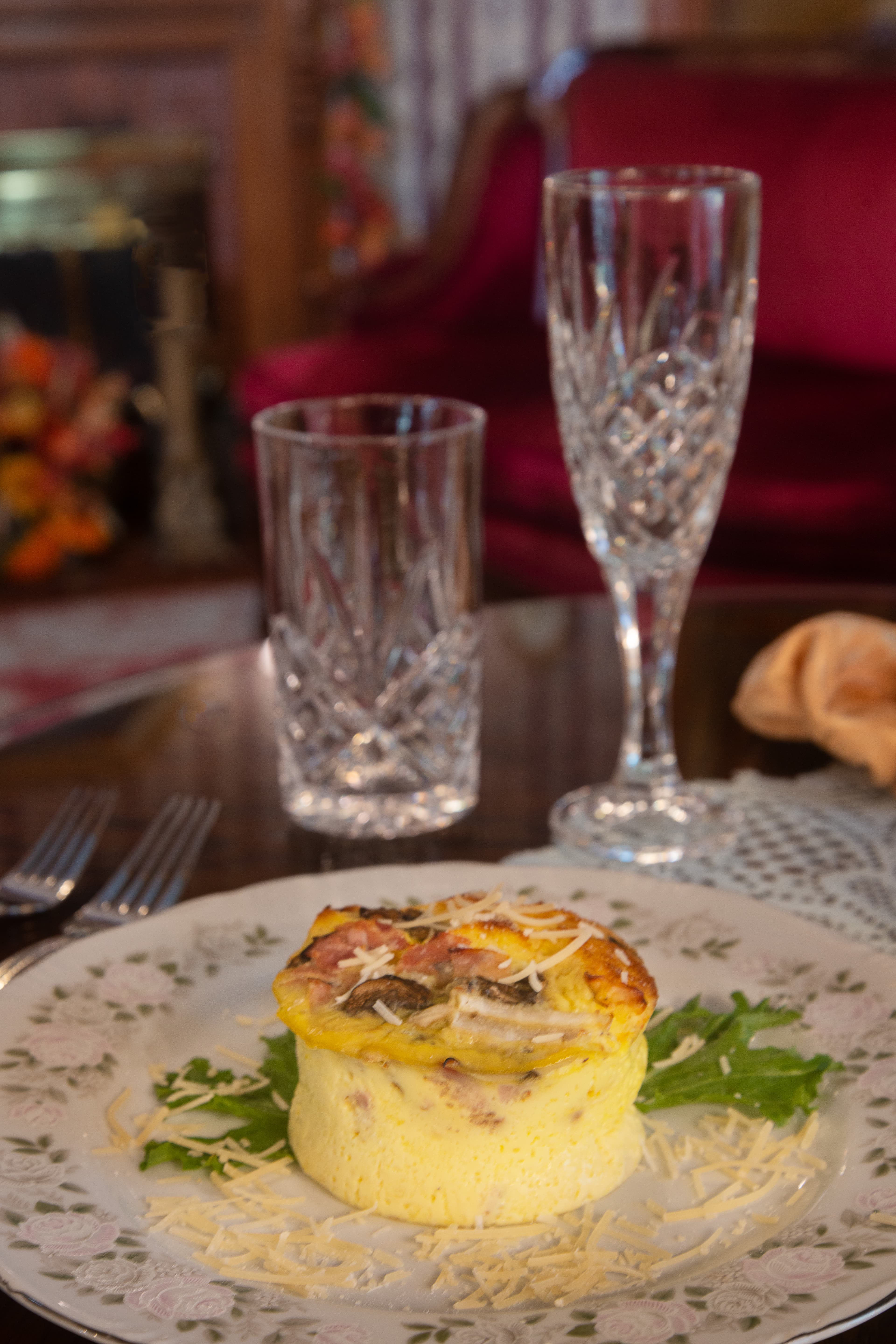 A plate with a fluffy omelet topped with cheese, sitting on a bed of greens, next to two glass tumblers.