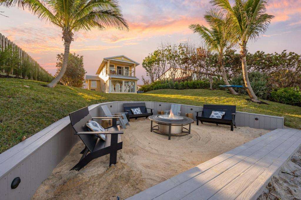 Cozy fire pit area surrounded by palm trees and a beach house under a colorful sunset.