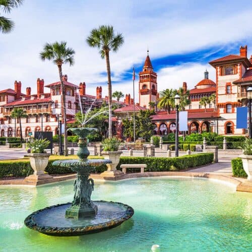 A historic building with a fountain and palm trees set against a clear blue sky.