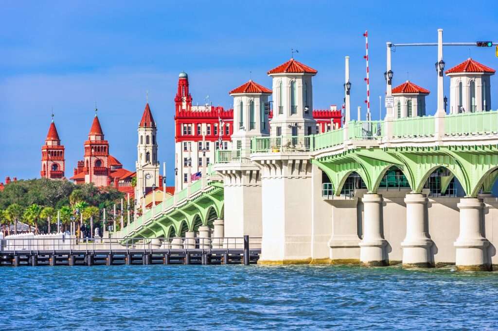 Historic buildings and a green bridge line the waterfront under a clear blue sky.