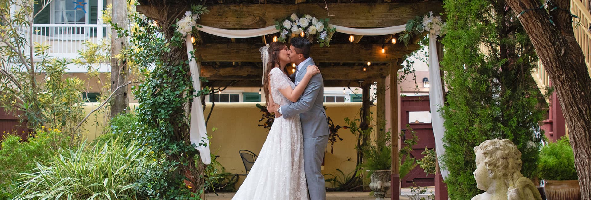 A couple kisses under a floral-adorned arbor during their wedding ceremony.