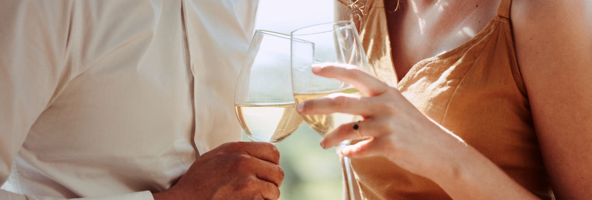 A close-up of two people clinking glasses of white wine.