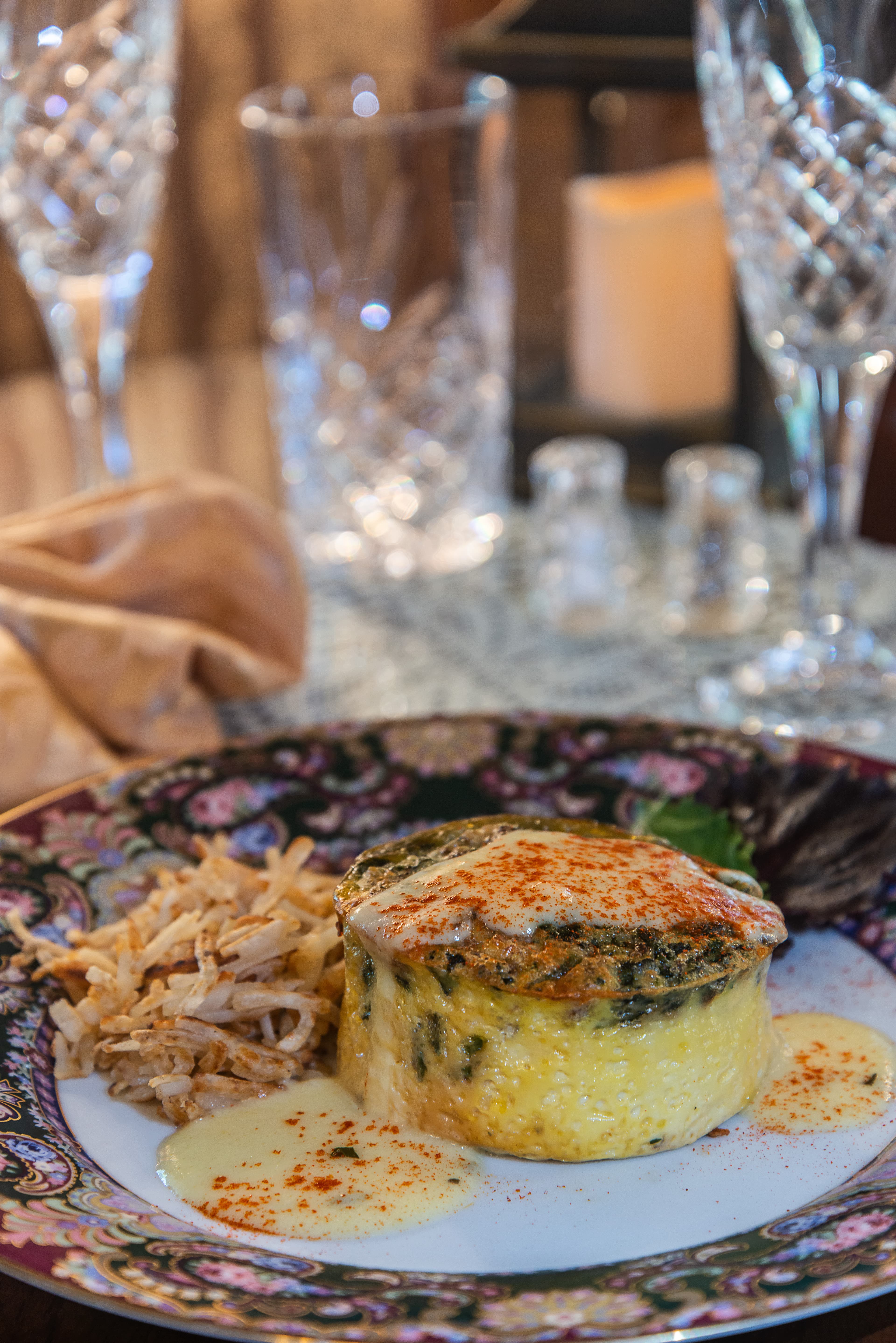 A colorful plate featuring a creamy spinach dish topped with paprika, alongside hash brown potatoes and a drizzle of sauce.