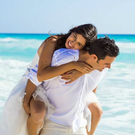 A joyful couple enjoying a beach piggyback ride against a vibrant ocean backdrop.