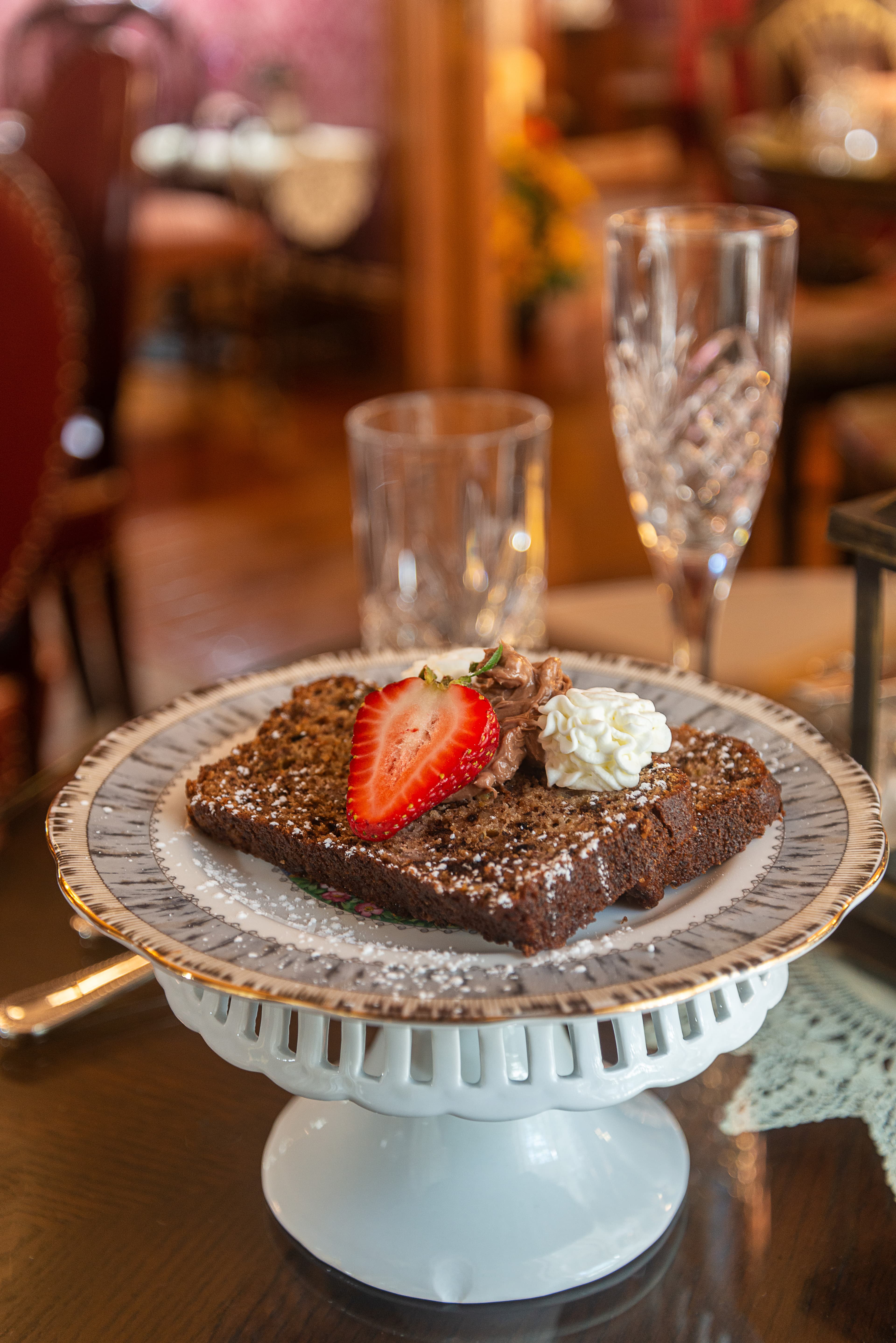 A slice of cake topped with a fresh strawberry, whipped cream, and a dollop of chocolate, served on a decorative plate.