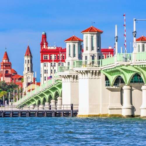 A green bridge spans a calm waterway, with colorful historic buildings in the background under a clear blue sky. A green bridge spans a calm waterway, with colorful historic buildings in the background under a clear blue sky.