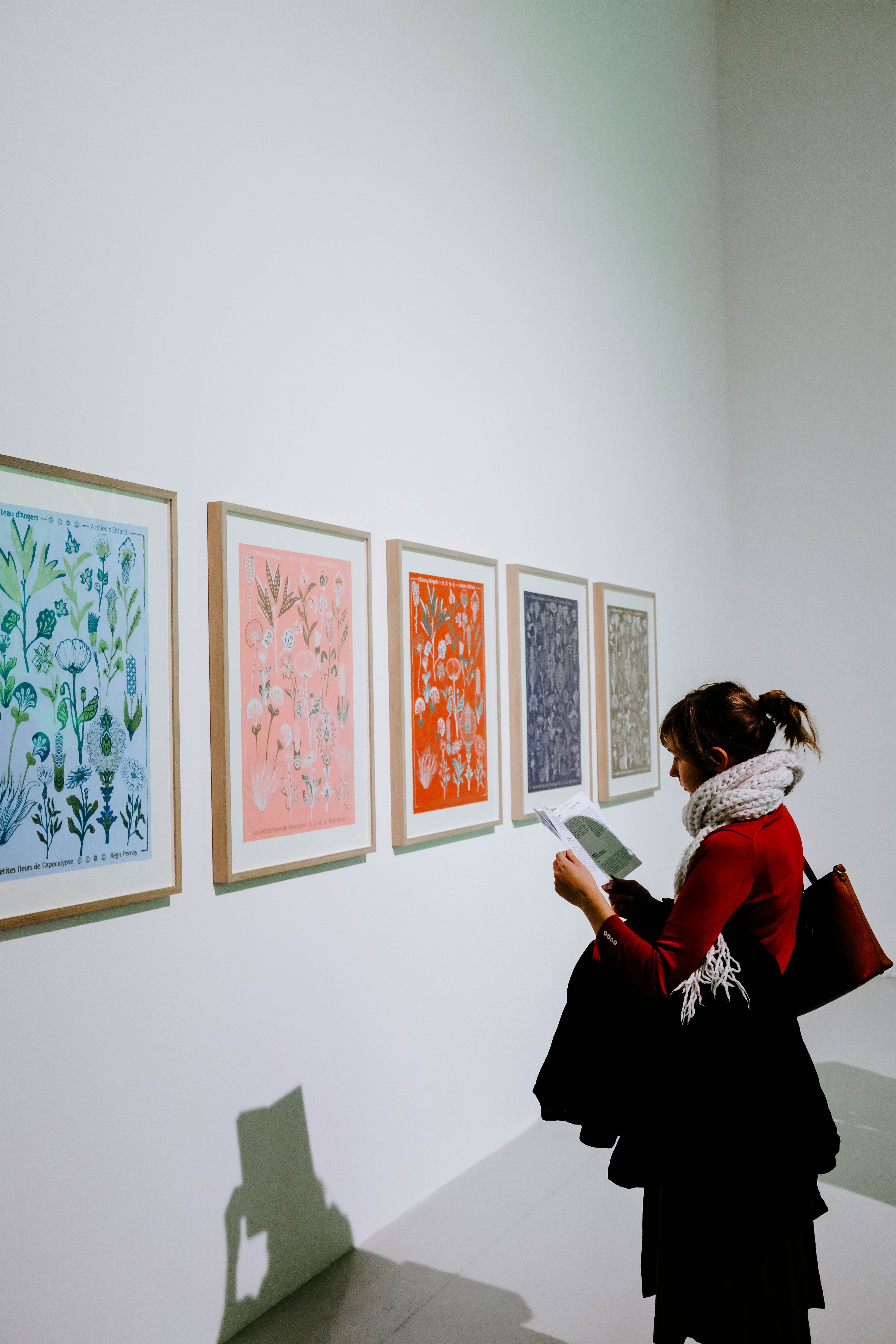 A woman stands in front of several art pieces hanging on a white wall.