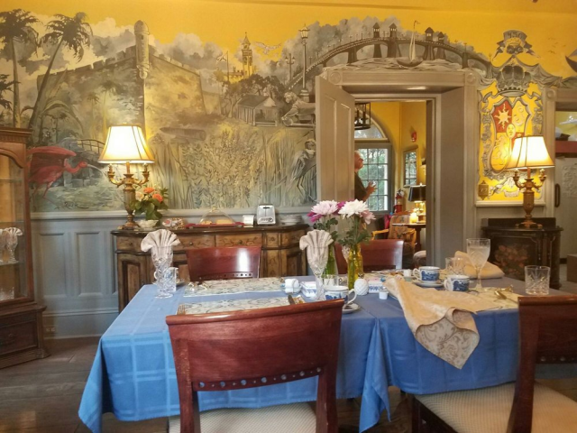 Beautiful table setting with a blue tablecloth. The walls of the room are yellow with a grey and blue mural of images of St. Augustine, FL.